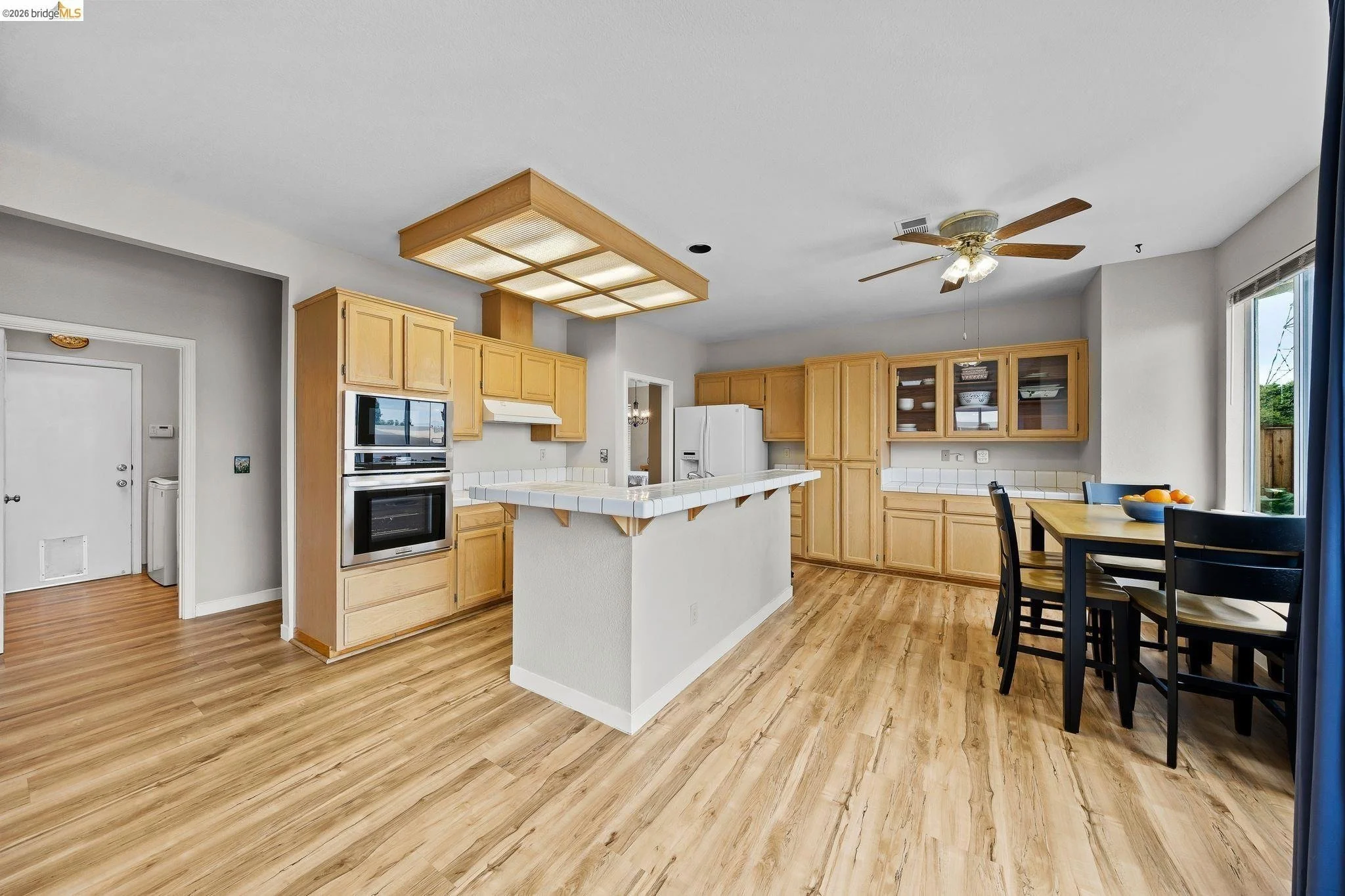 Kitchen with wooden cabinets, white appliances, a breakfast bar, a dining table with black chairs, and hardwood flooring.