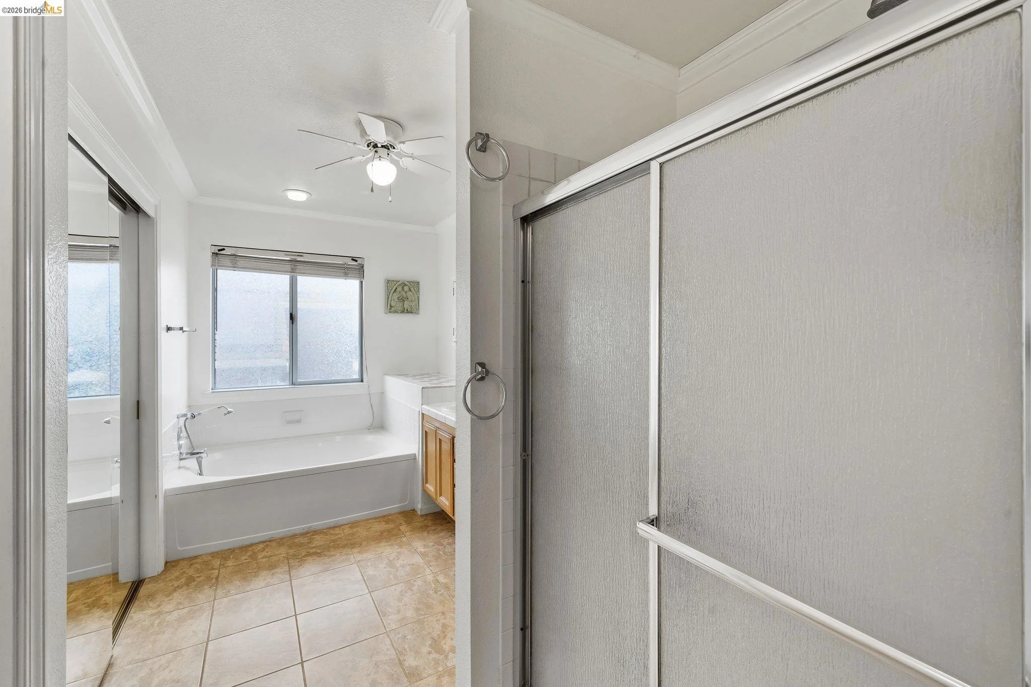 Bathroom with a bathtub near a window, a sliding shower door, and a ceiling fan.