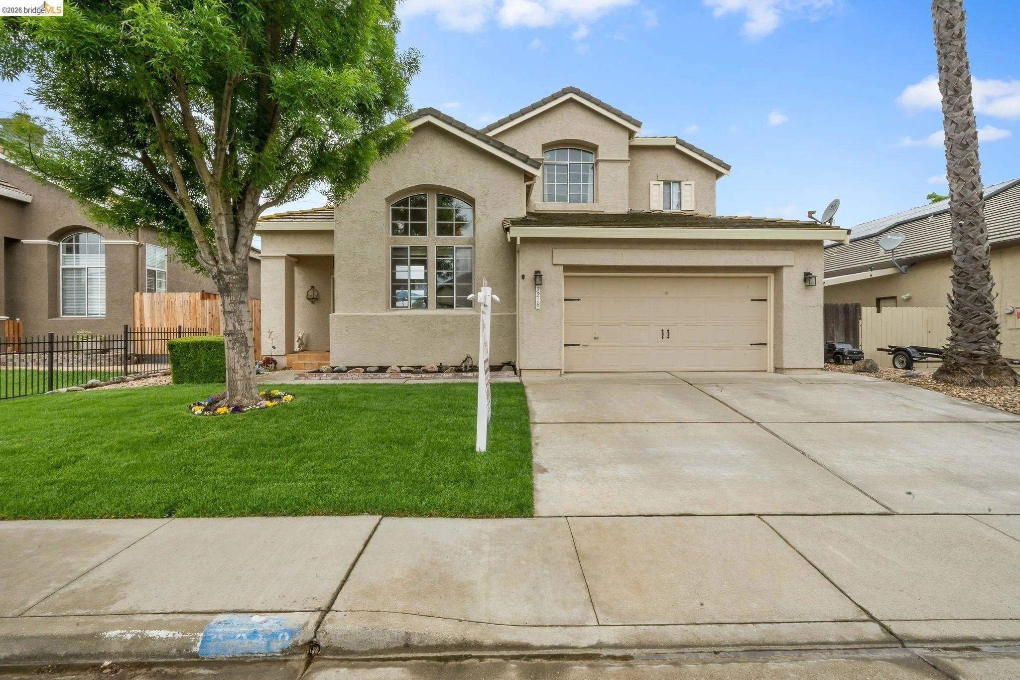 Front view of a two-story house with beige exterior, large arched window, attached garage, green lawn, and sidewalk.