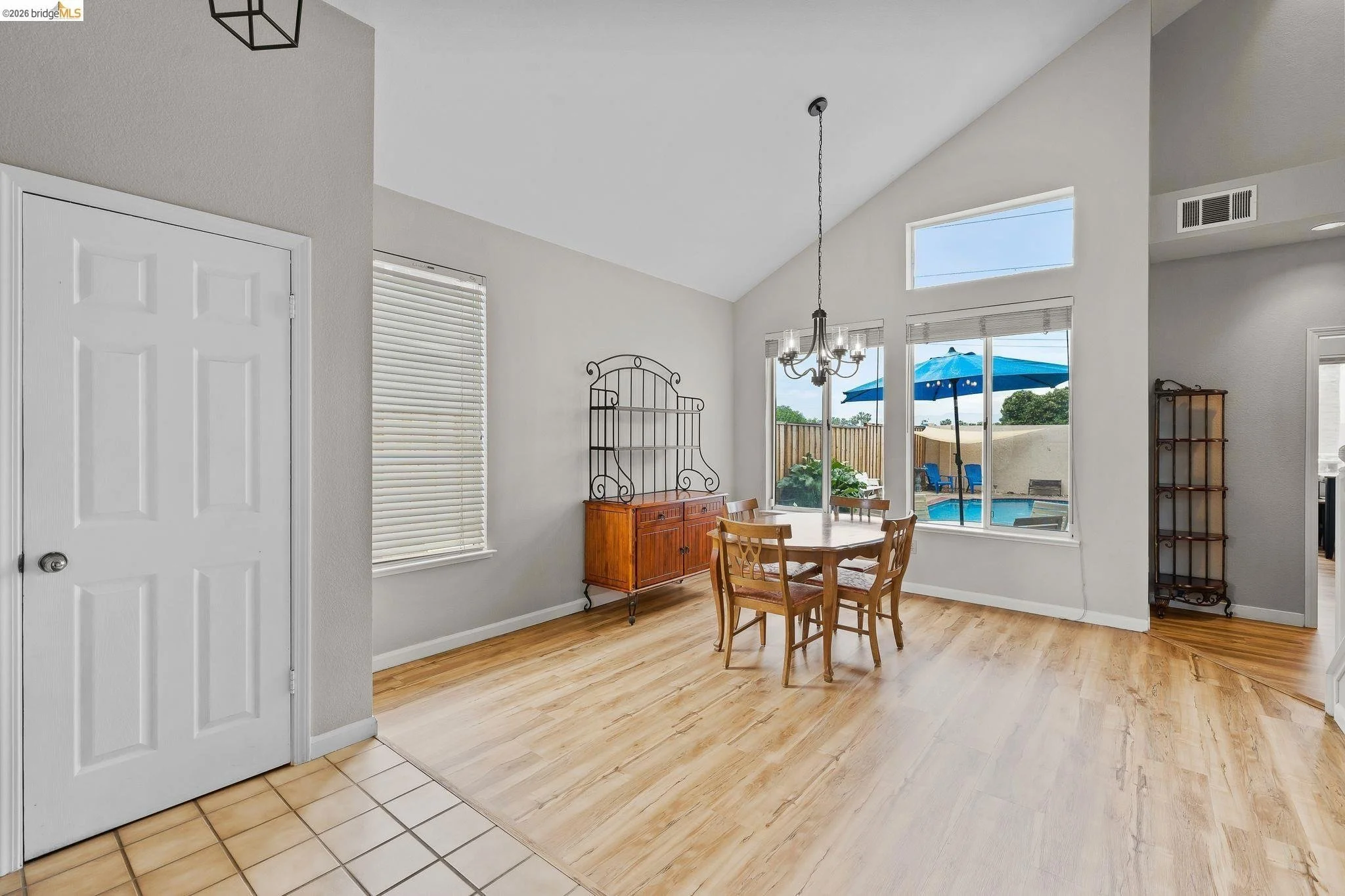 Dining area with wooden table and four chairs, large windows overlooking a backyard with a swimming pool, patio umbrella, and outdoor seating.