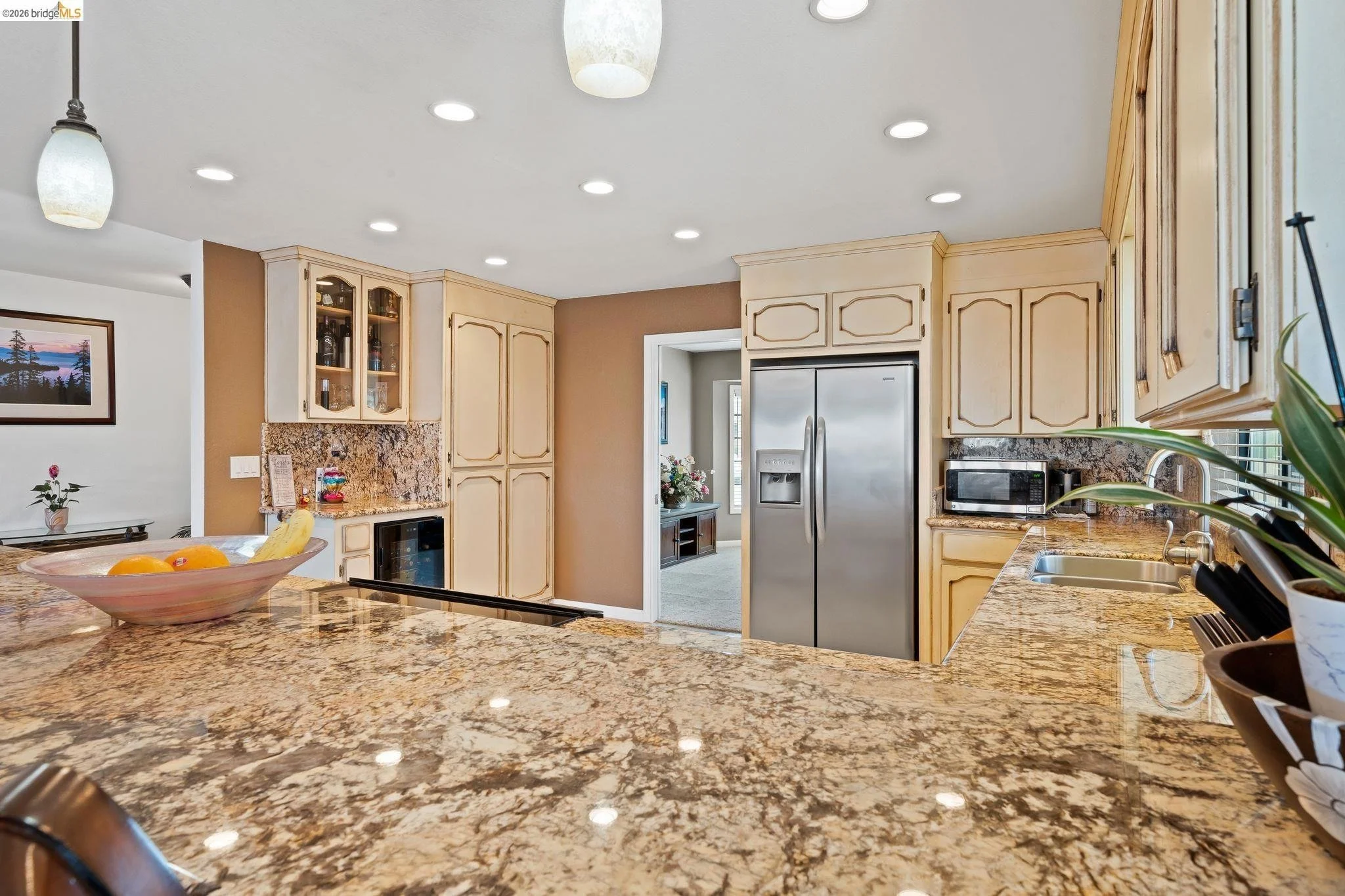 Kitchen with granite countertops, beige cabinets, stainless steel refrigerator, microwave, and a view into an adjacent room.