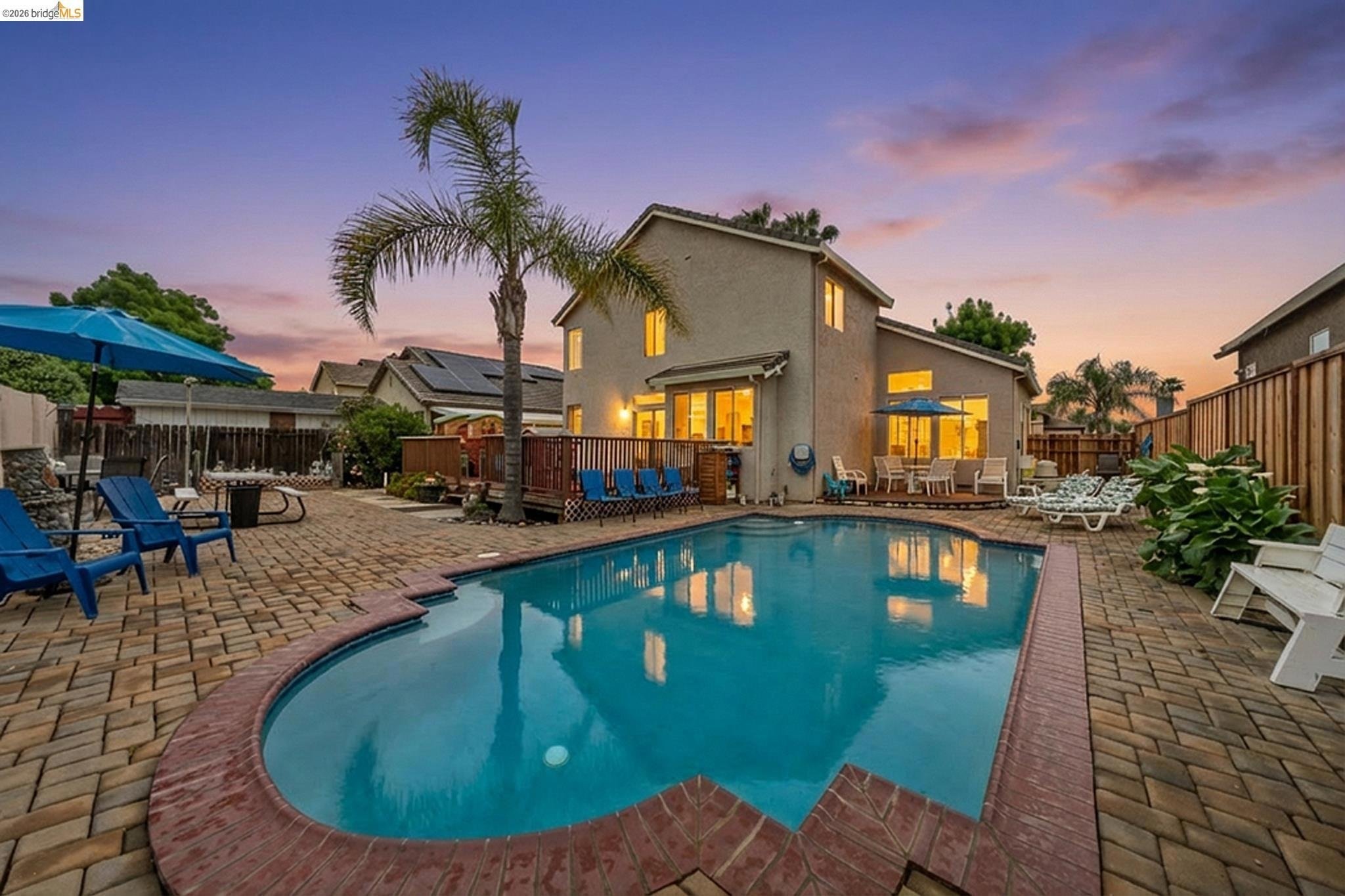 Backyard with swimming pool, palm tree, patio furniture, and house at sunset.