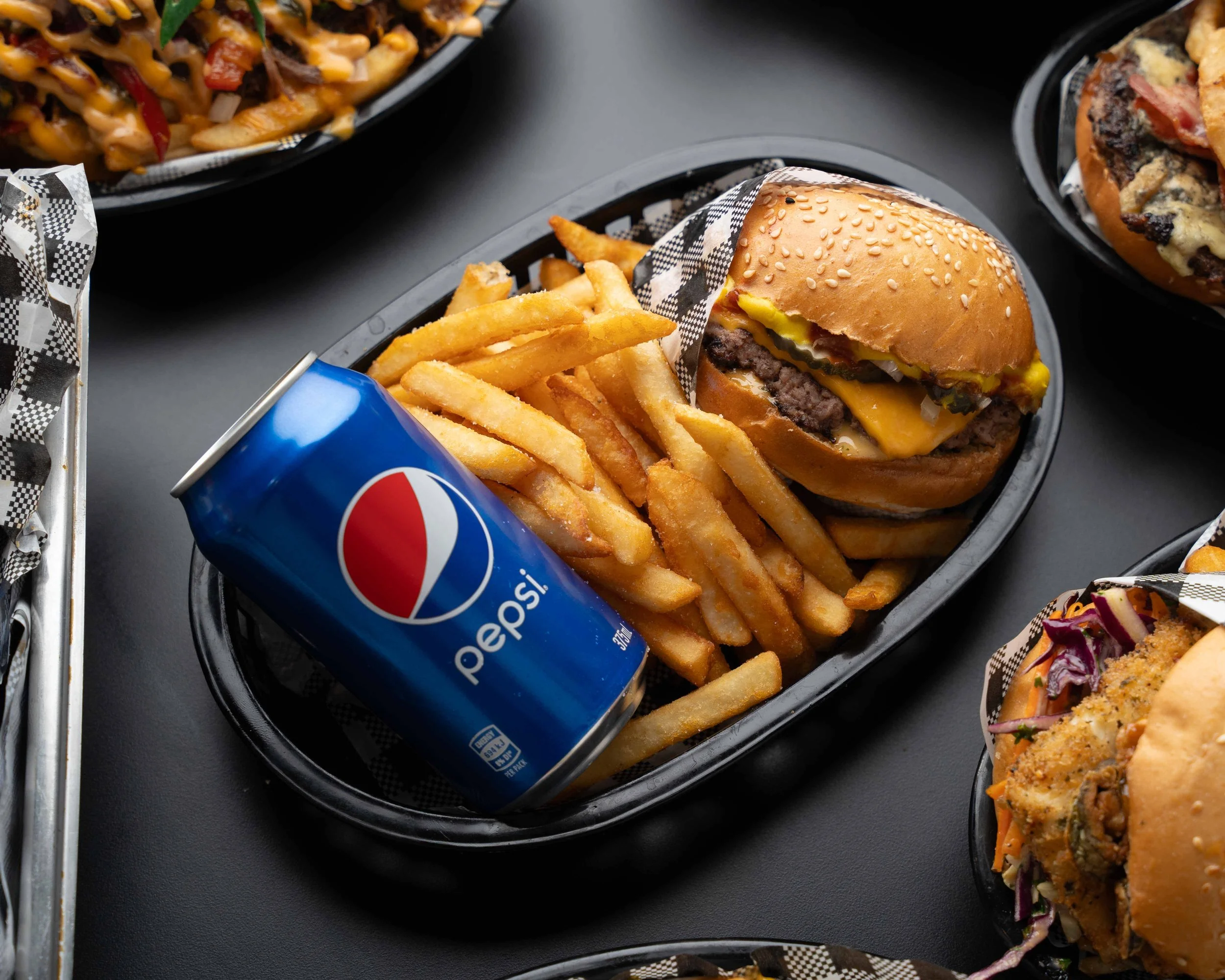 Fast food meal with cheeseburger, French fries, and a can of Pepsi in a black tray.