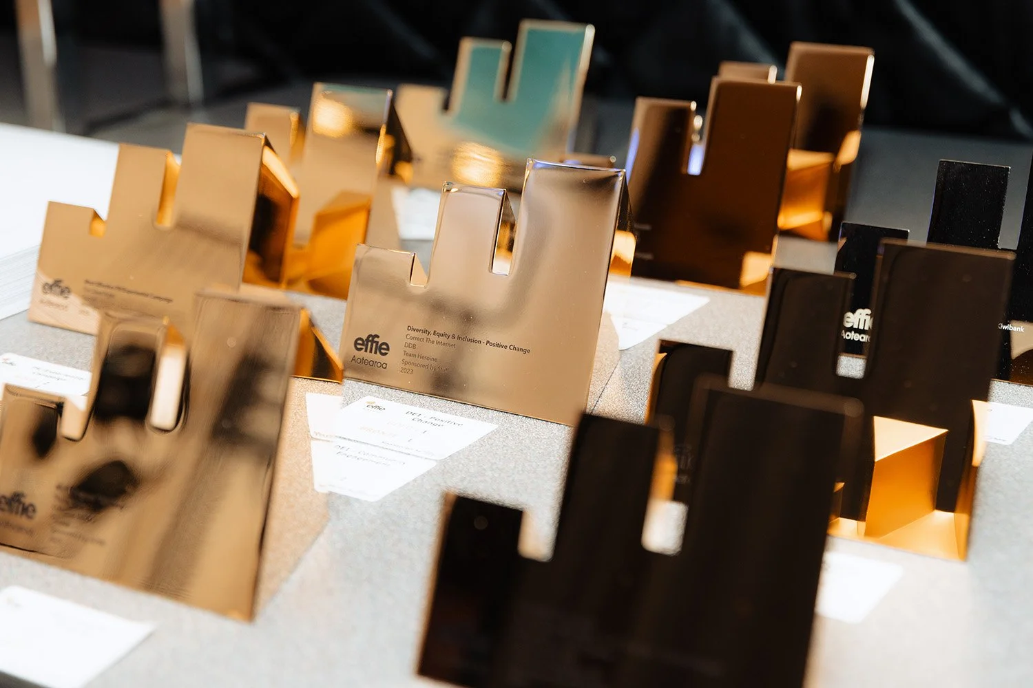 Various shiny, metallic awards for the Effies displayed on a table, some gold-colored, some black, with labels underneath.
