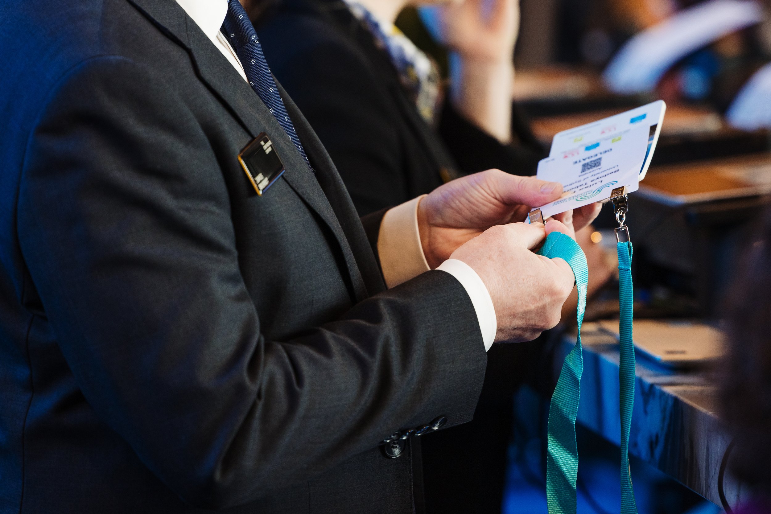 A person in a suit holding an airline boarding pass and a blue lanyard, seated on a plane with other passengers in the background.