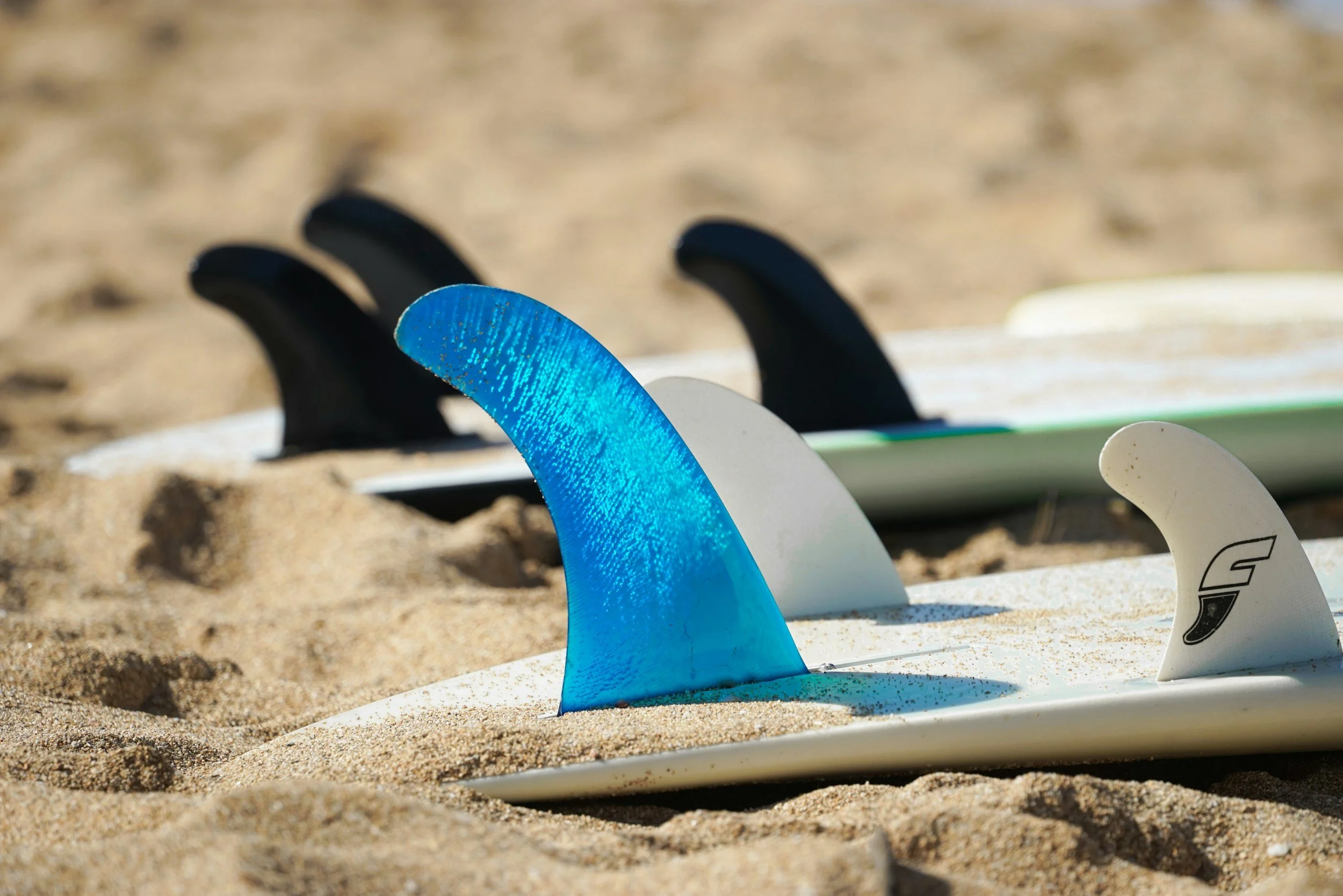 Several surfboards with fins sticking out of the sand at a beach.