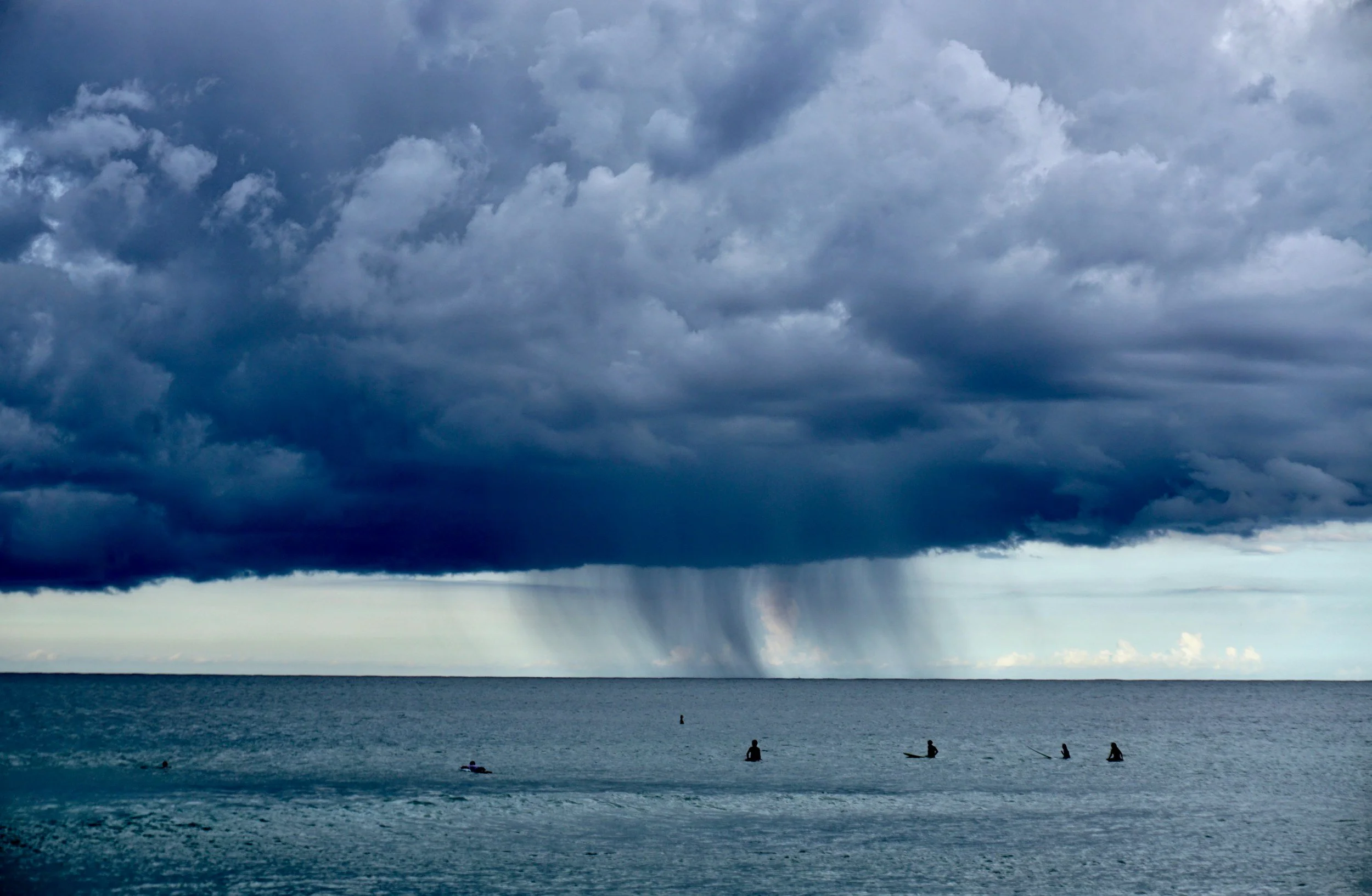 A dark storm cloud over the ocean with people in kayaks or small boats in the water below.
