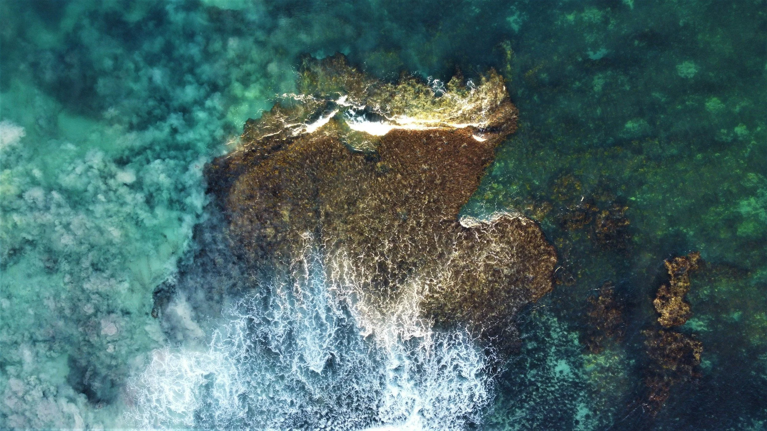 Aerial view of a rocky island surrounded by turquoise ocean water with waves crashing against the rocks.