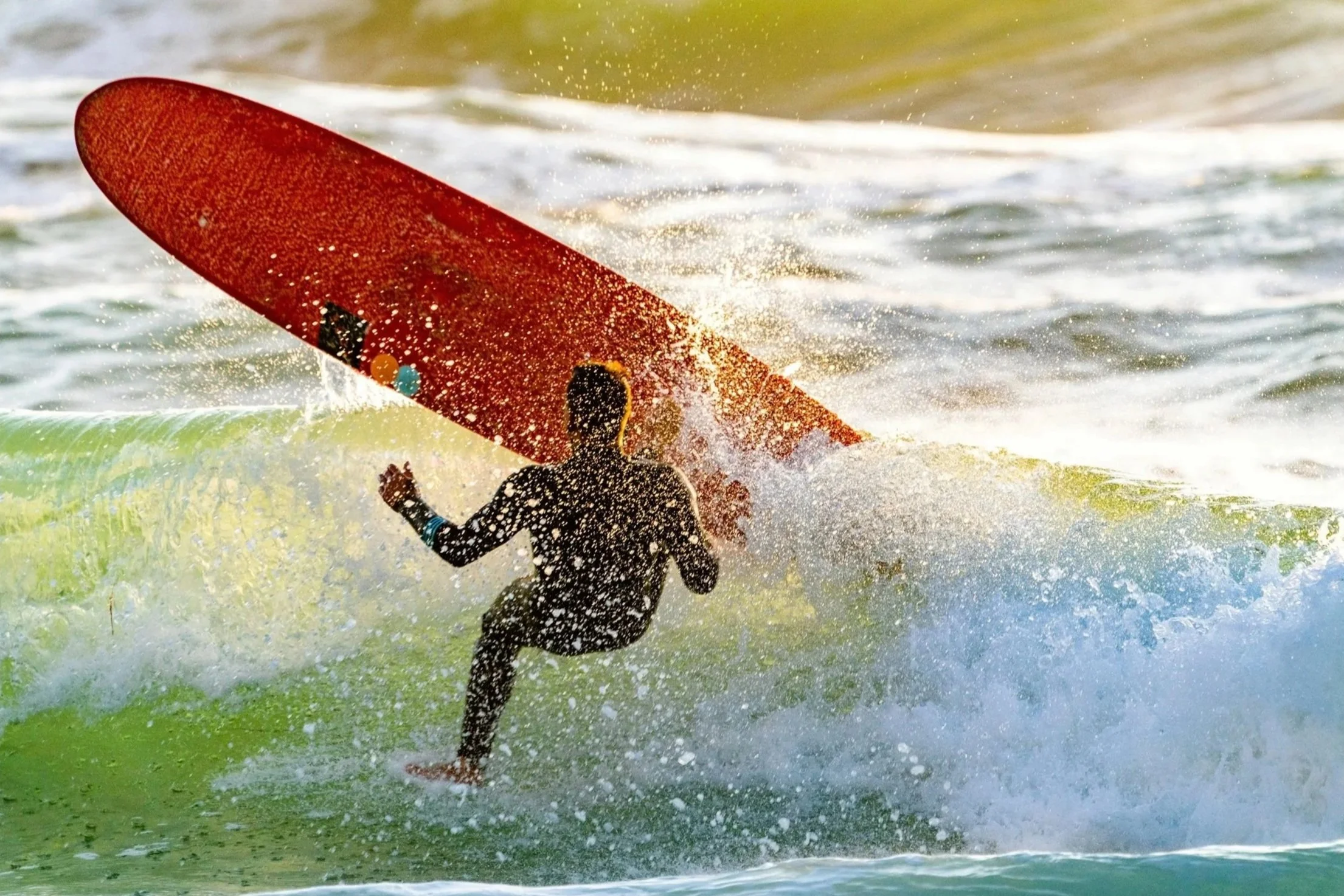 A person in a wetsuit surfing a wave with a red surfboard in the ocean.