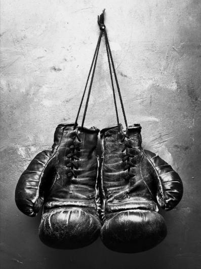 A pair of black boxing gloves hanging by their strings on a wall. Showing that we are willing to put aside differences to help athletes and student athletes