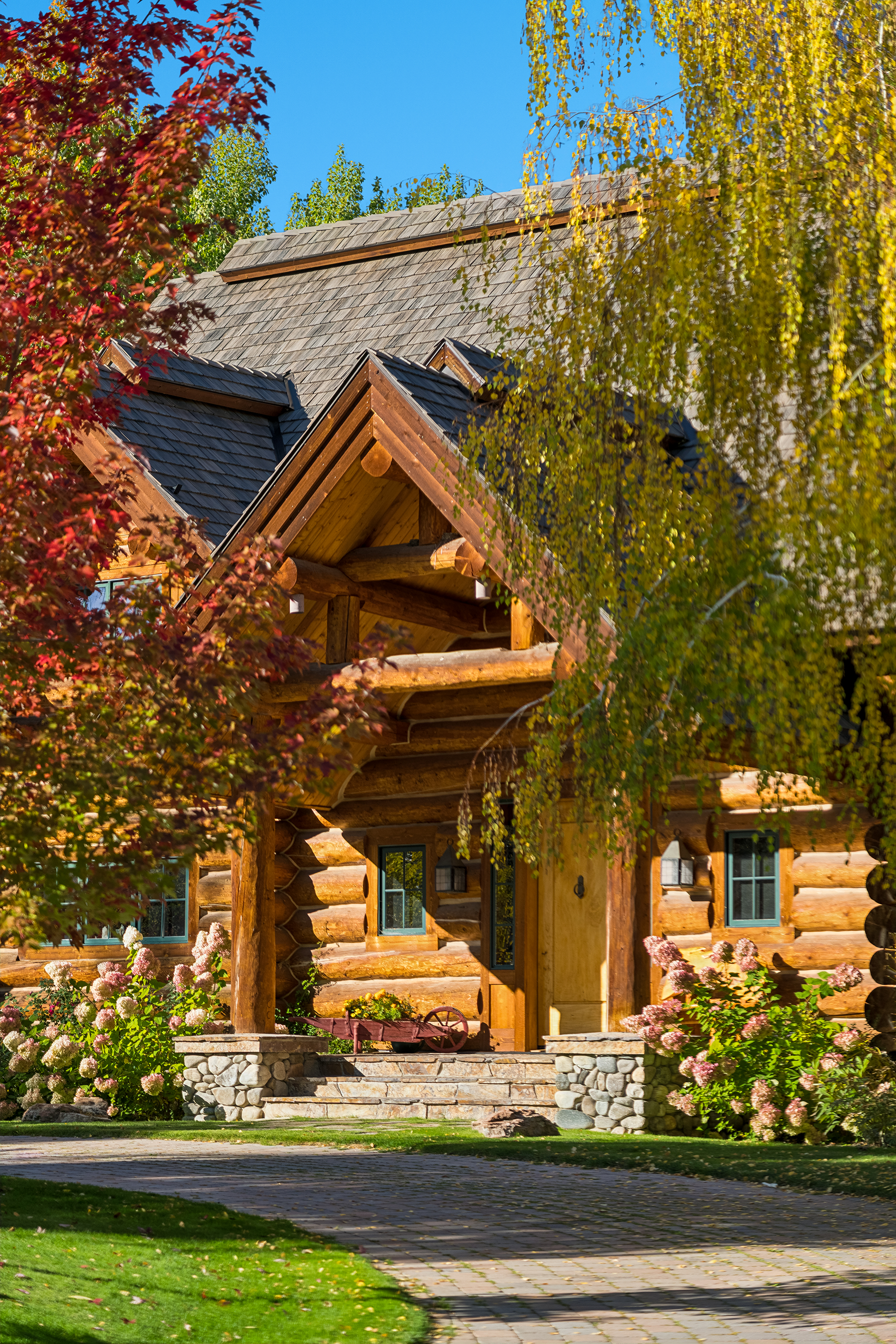 Brava synthetic slate roofing in charcoal gray on a luxury log home estate with stone foundation and mature landscaping, resort roofing Idaho Mountain West