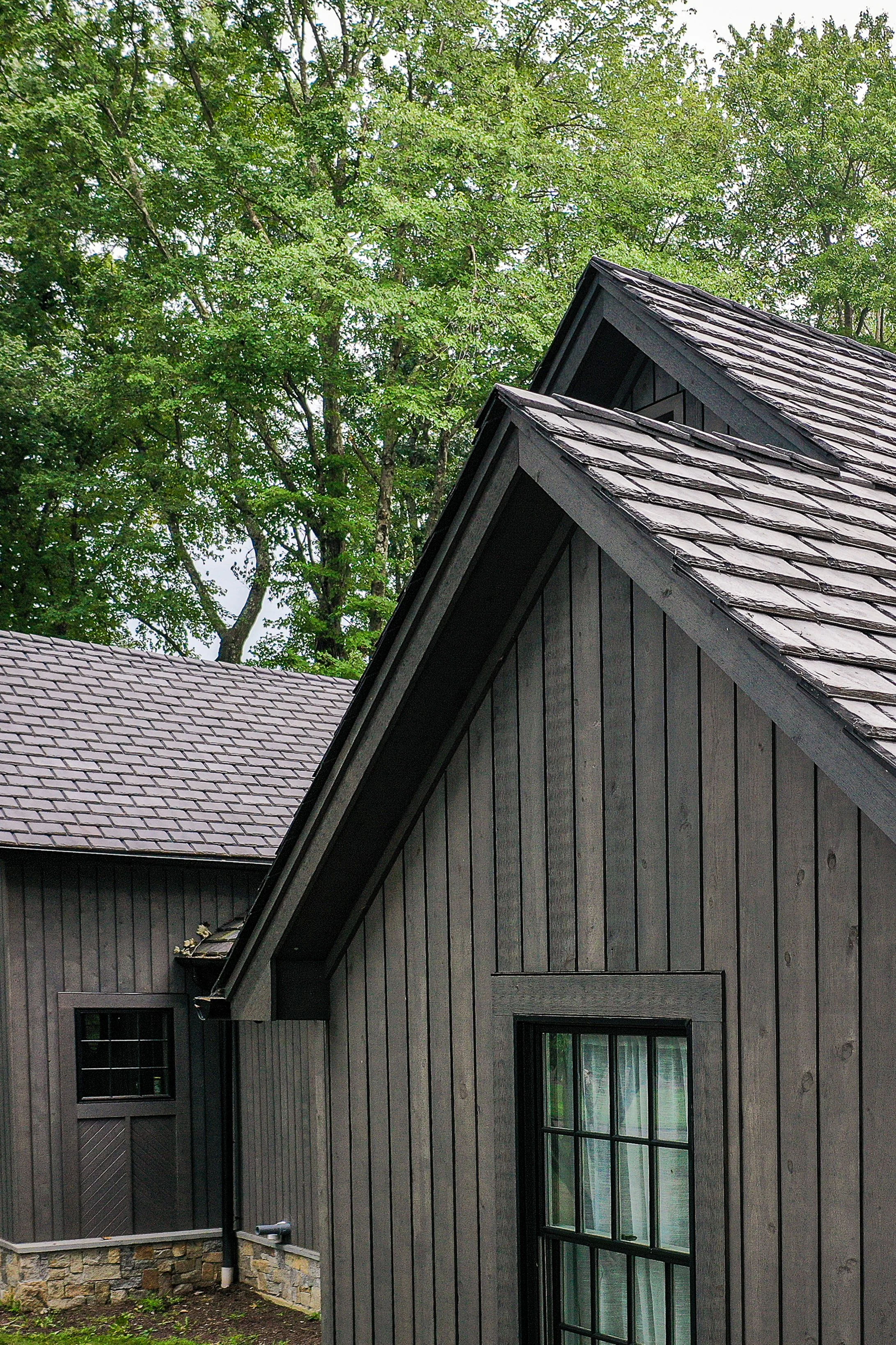 Brava Slate roofing in weathered gray on a dark board and batten farmhouse structure surrounded by mature trees, specialty roofing Idaho Mountain West