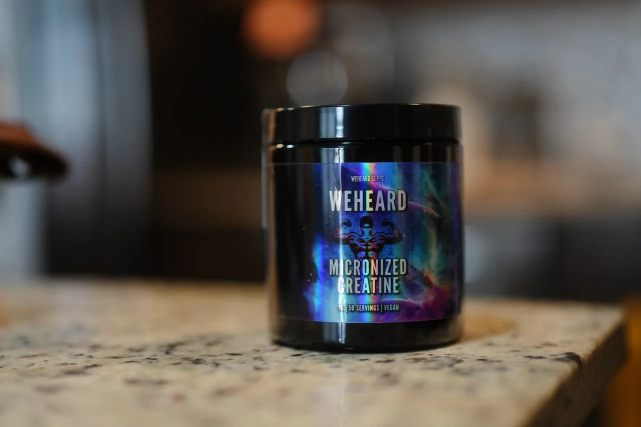 A black container of WeHeard Micronized Creatine sitting on a granite countertop in a kitchen setting.