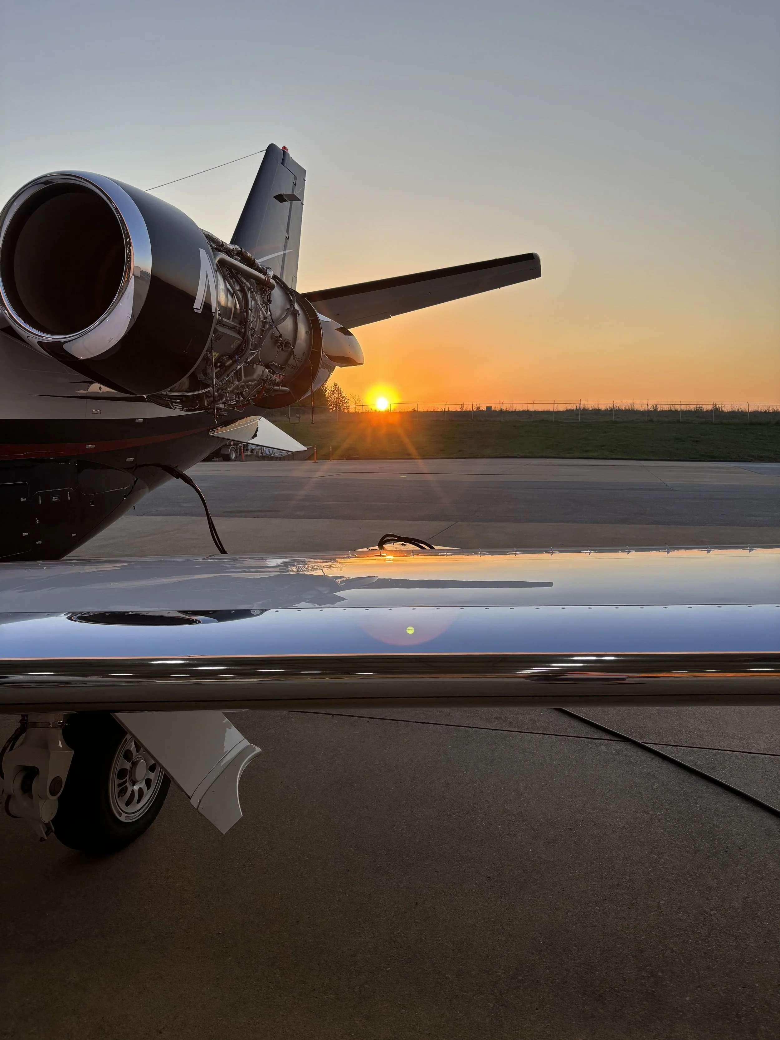 An aircraft parked on the tarmac during sunset, showing the engine and part of the wing.