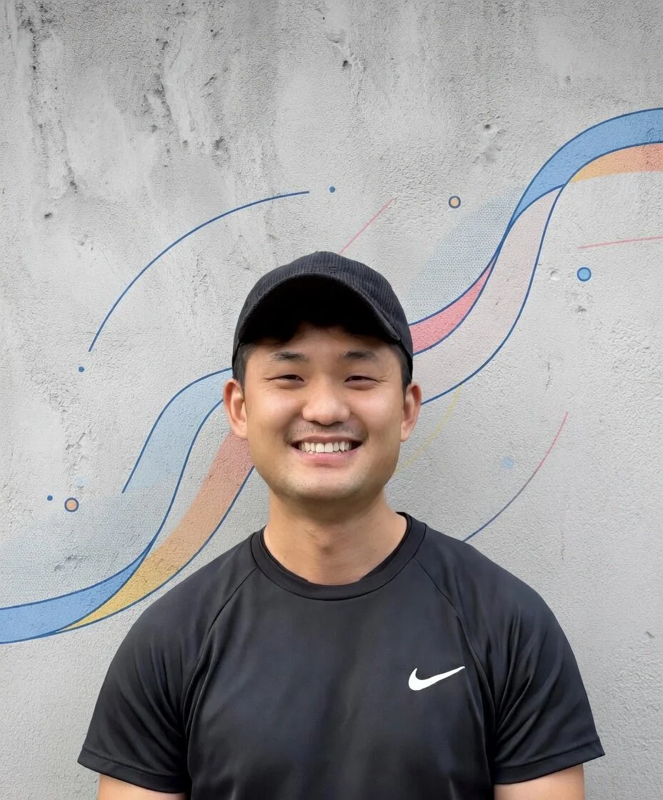 A smiling young man in a black Nike athletic shirt and cap standing in front of a painted wall with colorful abstract lines.