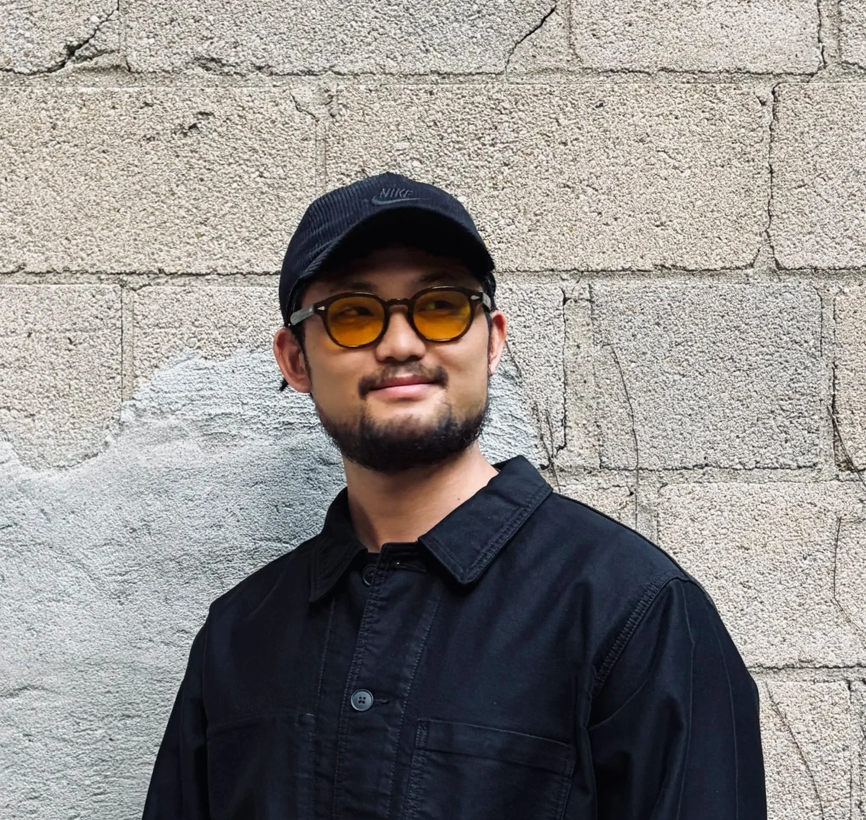 A smiling young man in a black Nike athletic shirt and cap standing in front of a painted wall with colorful abstract lines.