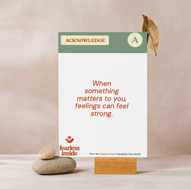 A printed acknowledgment card with a motivational quote that says, "When something matters to you, feelings can feel strong." The card has a green and white header labeled "ACKNOWLEDGE" with a letter "A," and is supported on a small wooden stand. The