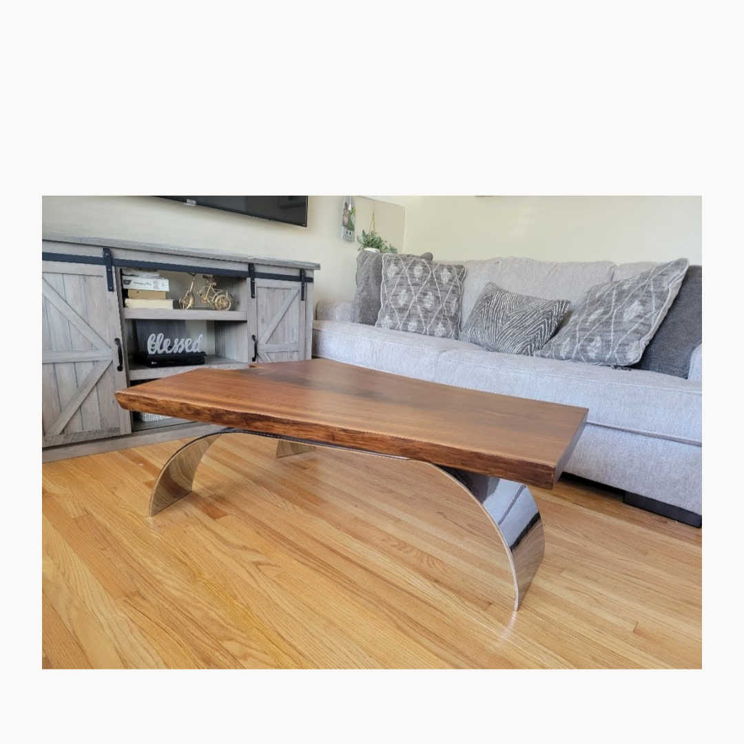 A living room with a wooden coffee table with a curved metal base, a gray couch with decorative pillows, and a rustic wooden entertainment console with decor items on it.
