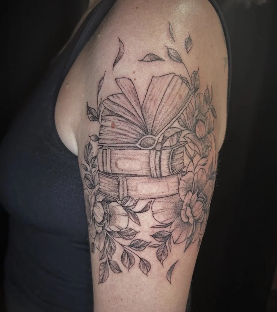 A tattoo of a vintage camera surrounded by flowers and leaves on a person's upper arm.
