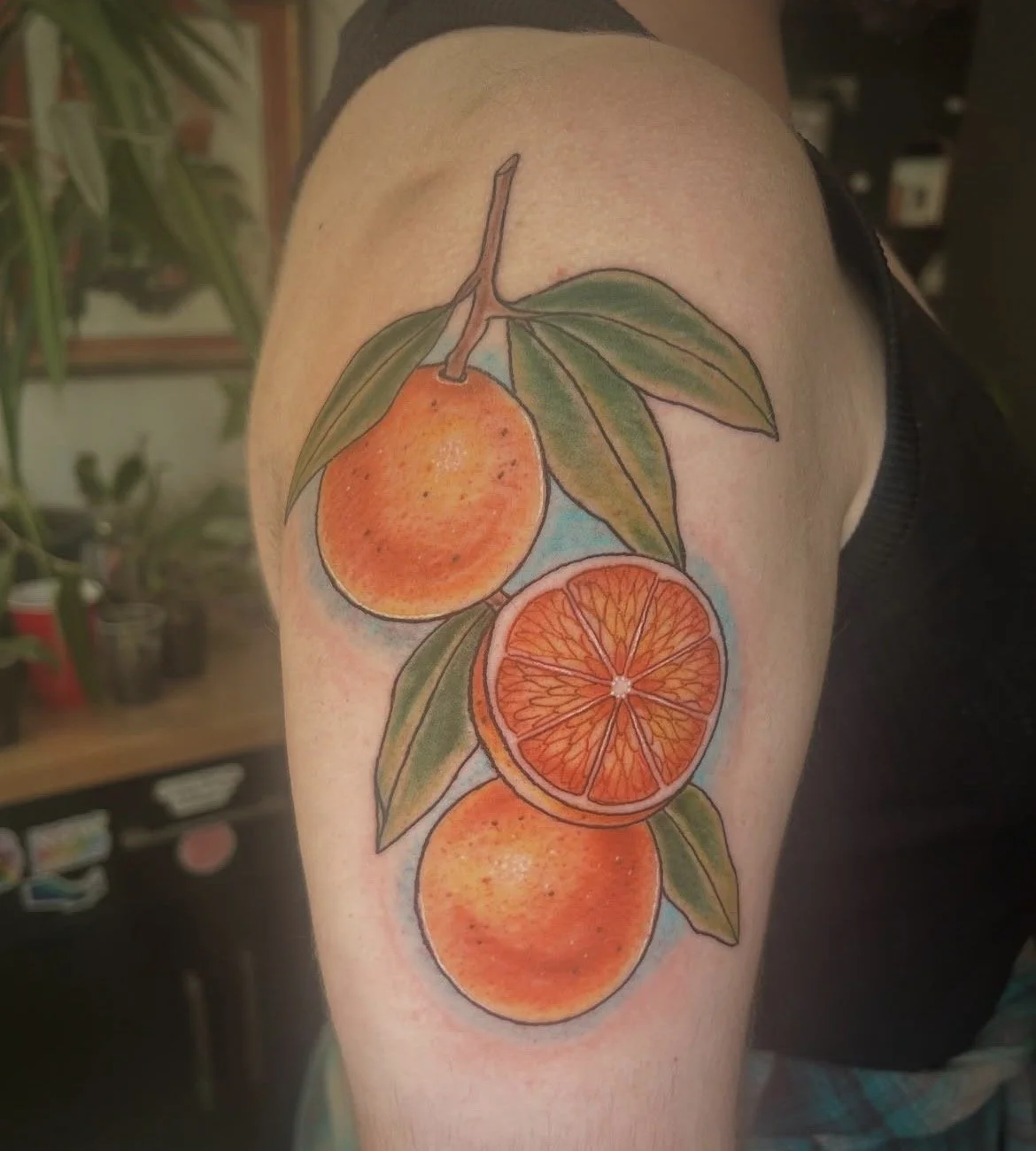 Colorful tattoo of three oranges on a branch with green leaves.