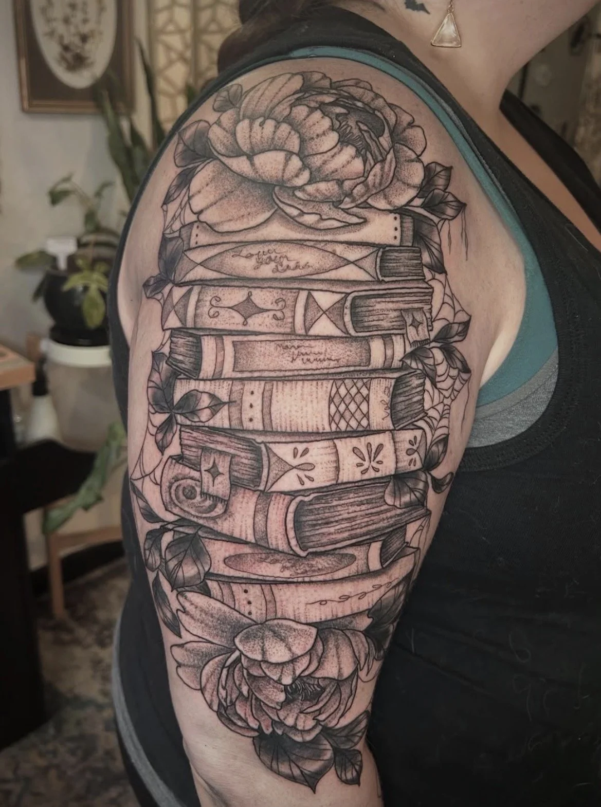 Black and gray tattoo of stacked books with floral elements on person's upper arm.