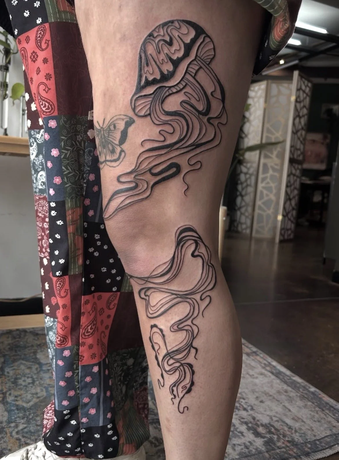 Tattoo of a mushroom with stylized, flowing lines on a person's thigh.