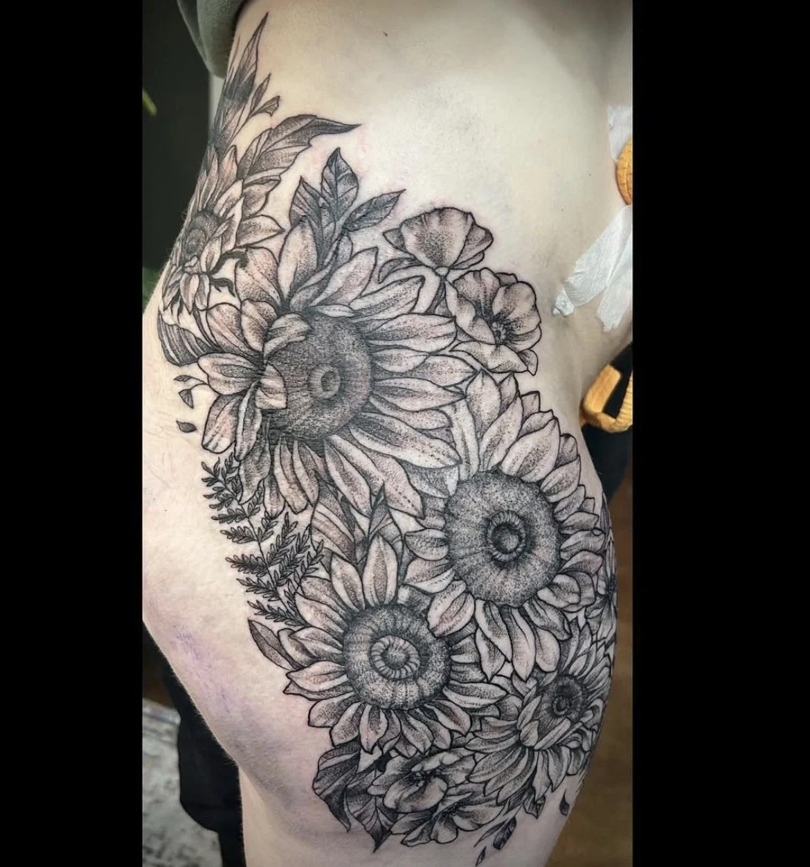 Black and white tattoo of sunflowers and other flowers on a person's side and ribs.