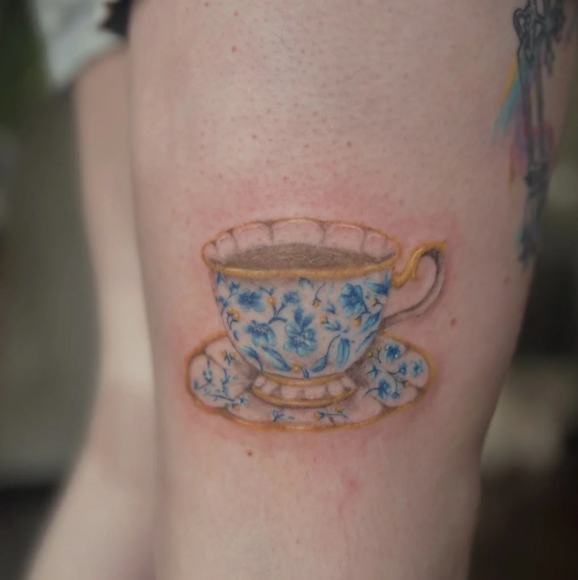 Tattoo of a teacup with a floral pattern on someone’s arm.