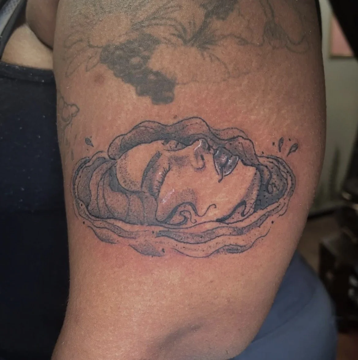 Tattoo of a sliced open avocado on person's upper arm.