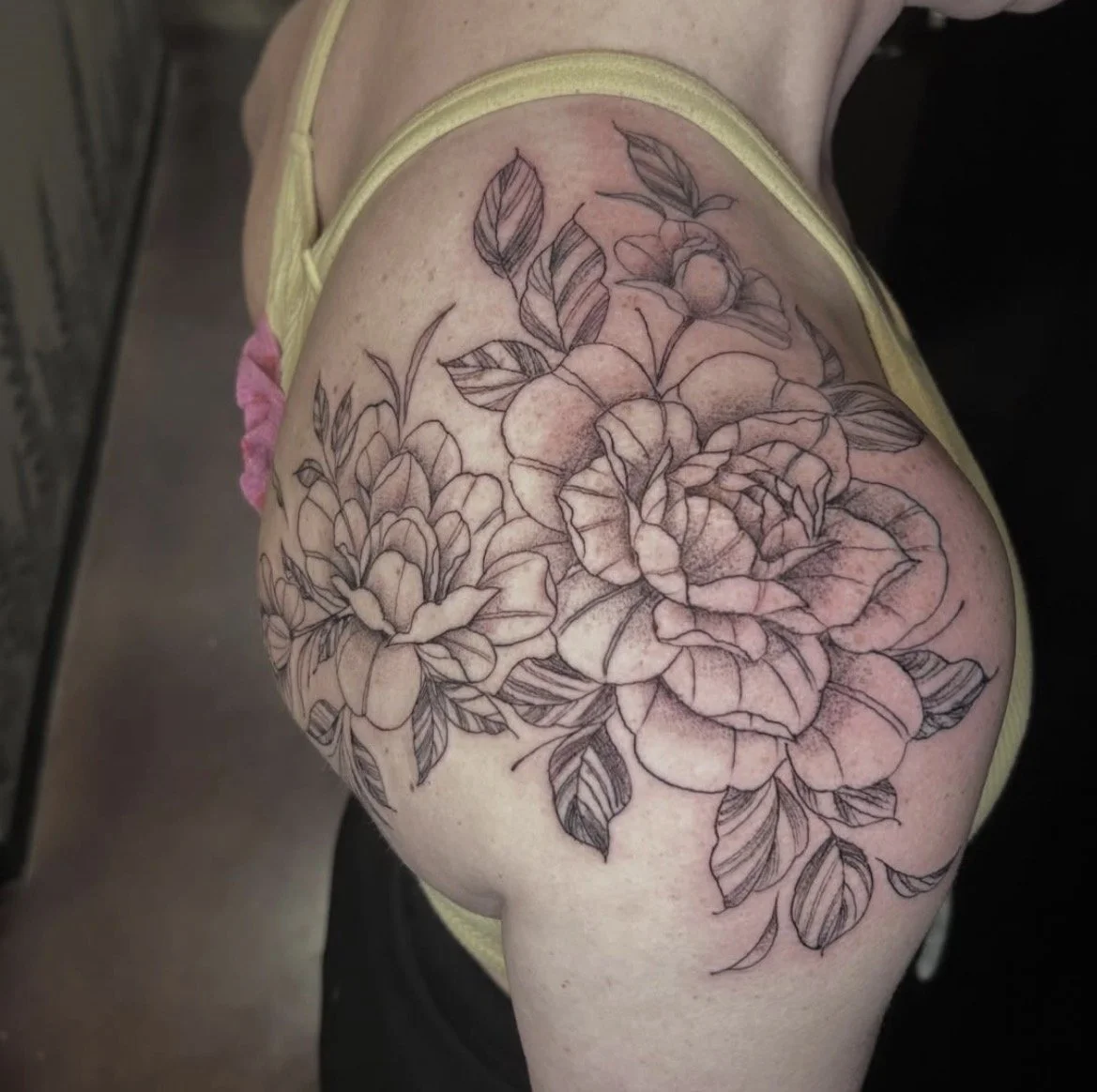 A black and white outline floral tattoo featuring large roses and leaves on a person's shoulder.