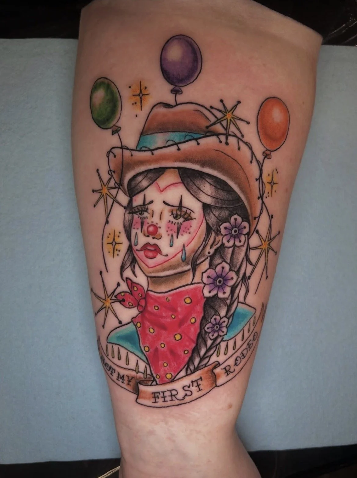 Tattoo of a sad clown girl with a hat, flowers in her hair, tears on her face, and a banner reading "First My Furest" with balloons and stars.