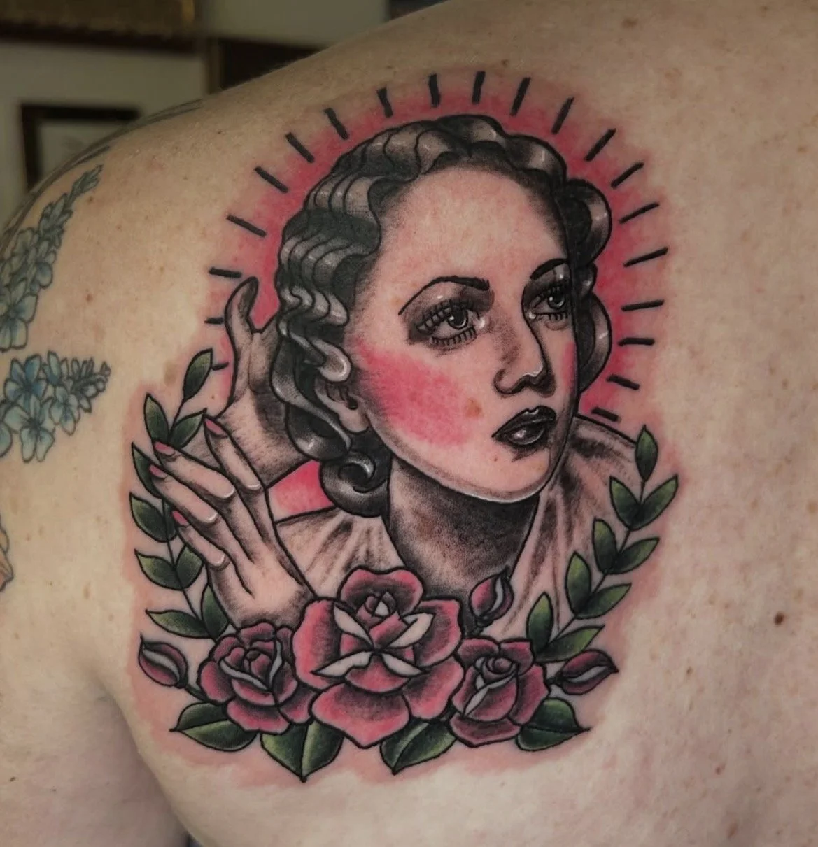 A colorful tattoo of a woman with curly hair, surrounded by roses and leaves, with a pink glow and radiating lines behind her head.