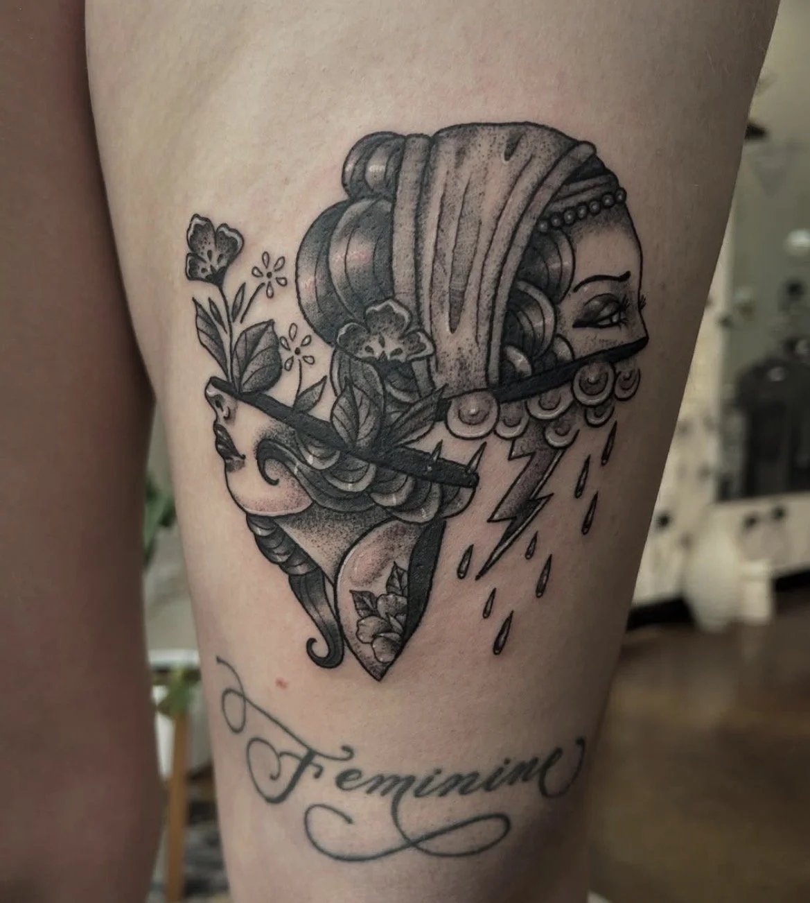 Black and gray tattoo of a woman's profile with decorative floral and lightning bolt elements, and the word 'Feminine' written below.