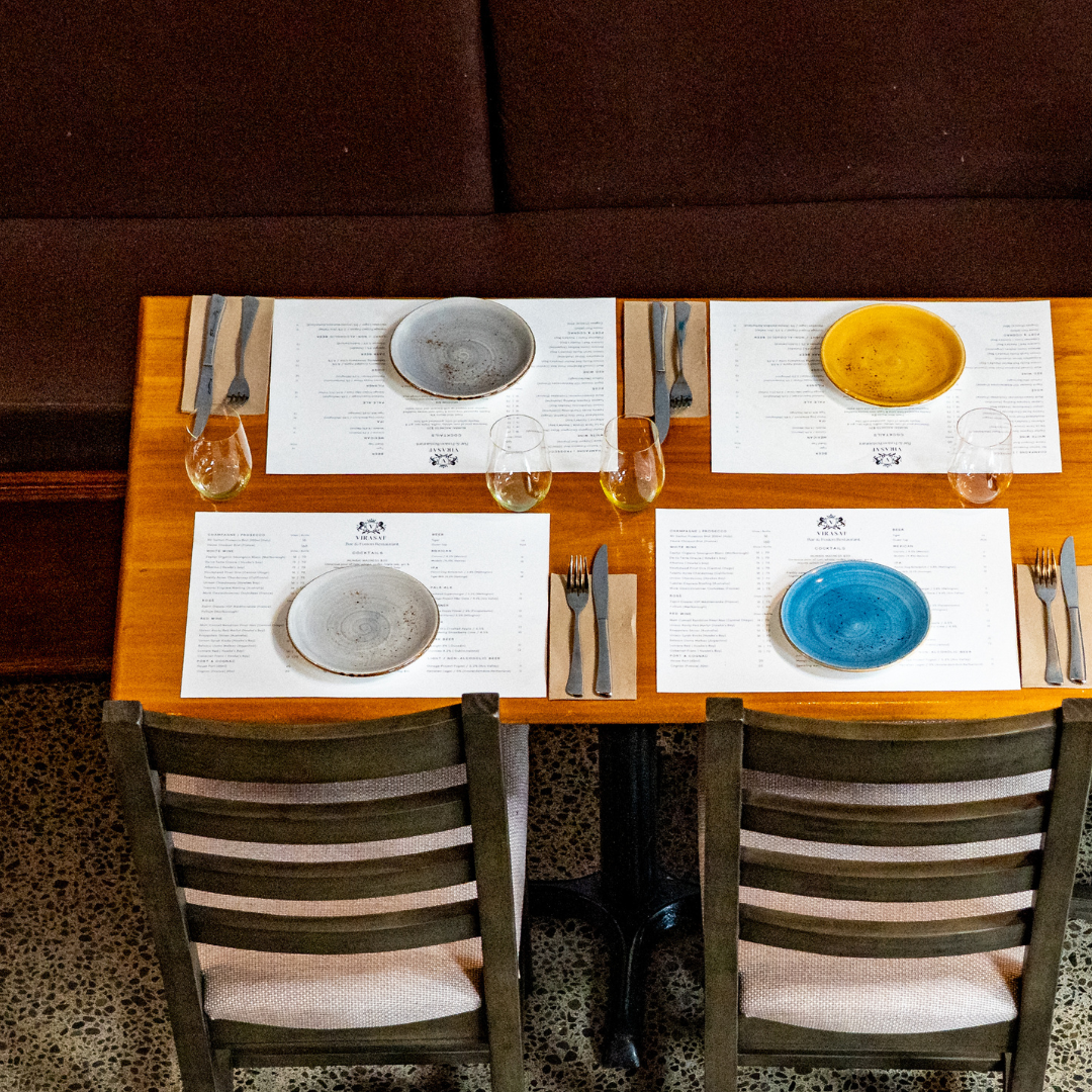 A table set for four with colored plates, glasses of water or wine, and utensils, in a restaurant.