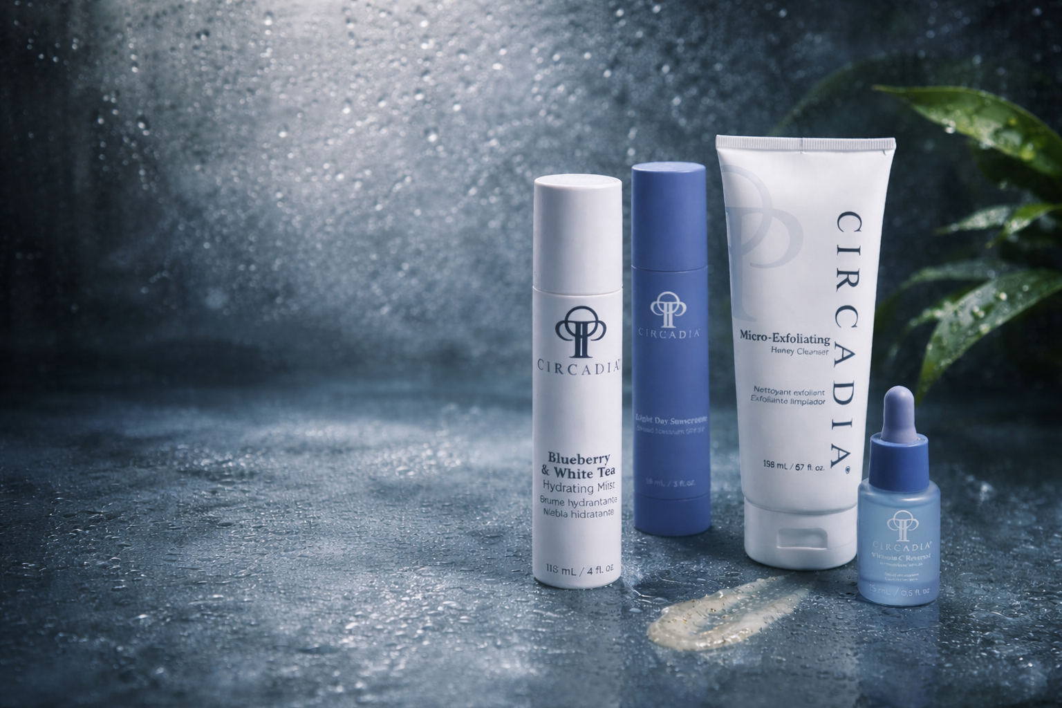 Skincare products including a blue and white moisturizer, a blue facial sunscreen, a white cleanser tube, and a small blue serum dropper bottle with the Circadia logo on a wet surface with water droplets, a smear of cream, and green leaves on the right.