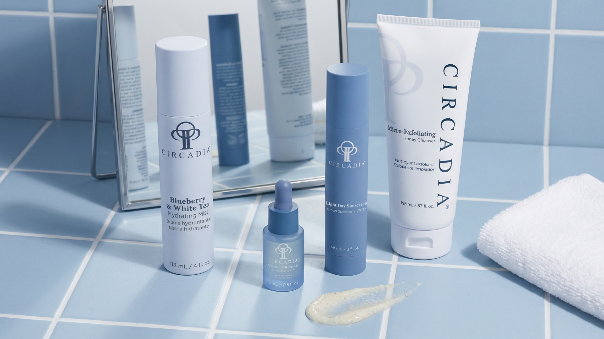 A collection of Circadia skincare products on a bathroom countertop, including mist, sunscreen, a vitamin C serum, honey cleanser, and a white towel, with a mirror reflecting the products.
