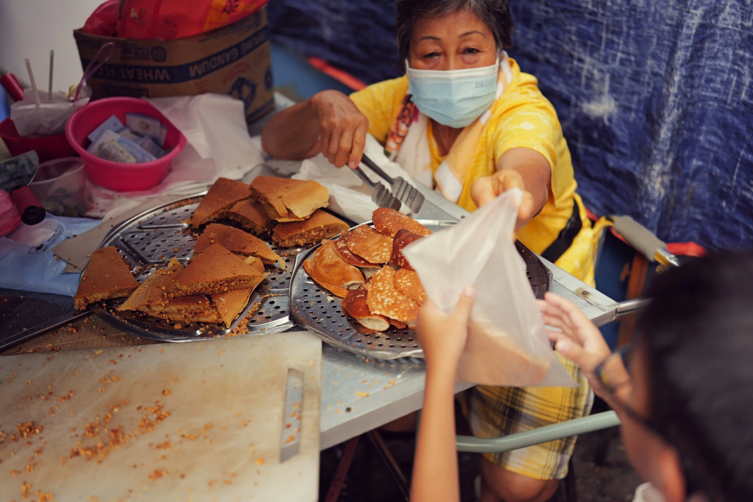 A vendor hands a bag across a stall piled with golden pastries.