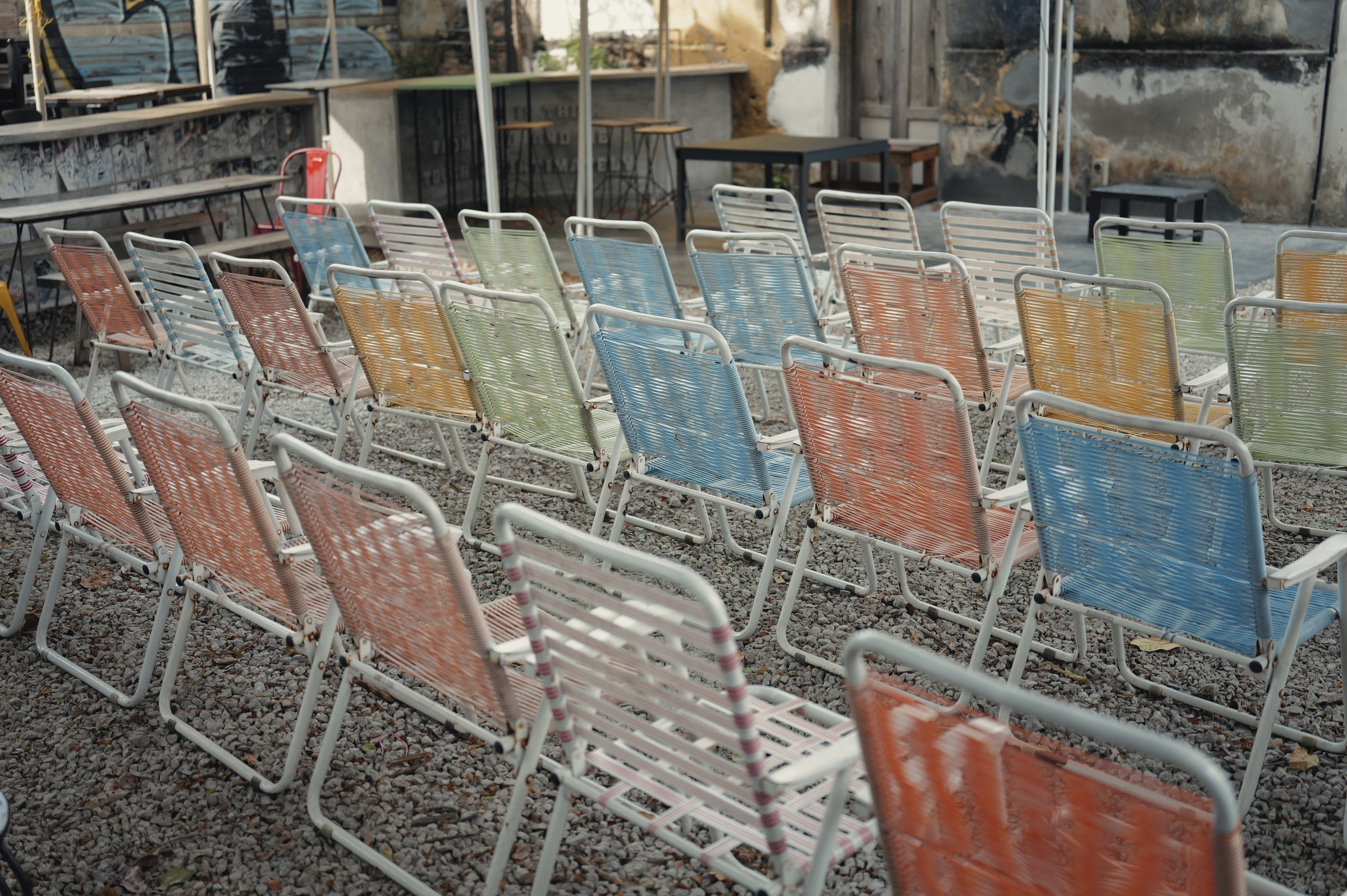 Rows of pastel folding chairs stand in a gravel courtyard.
