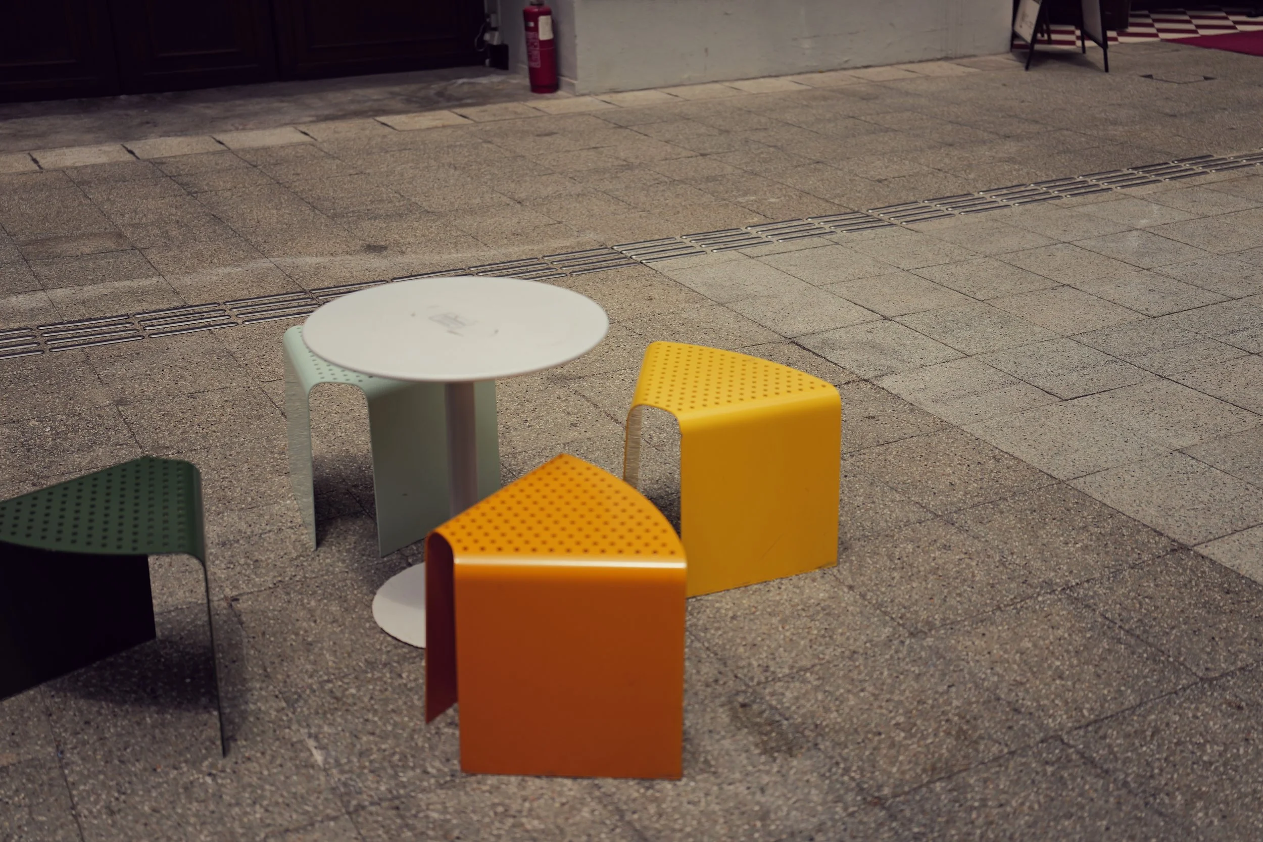 Colorful outdoor seating with modern chairs and a small round table on a paved sidewalk.