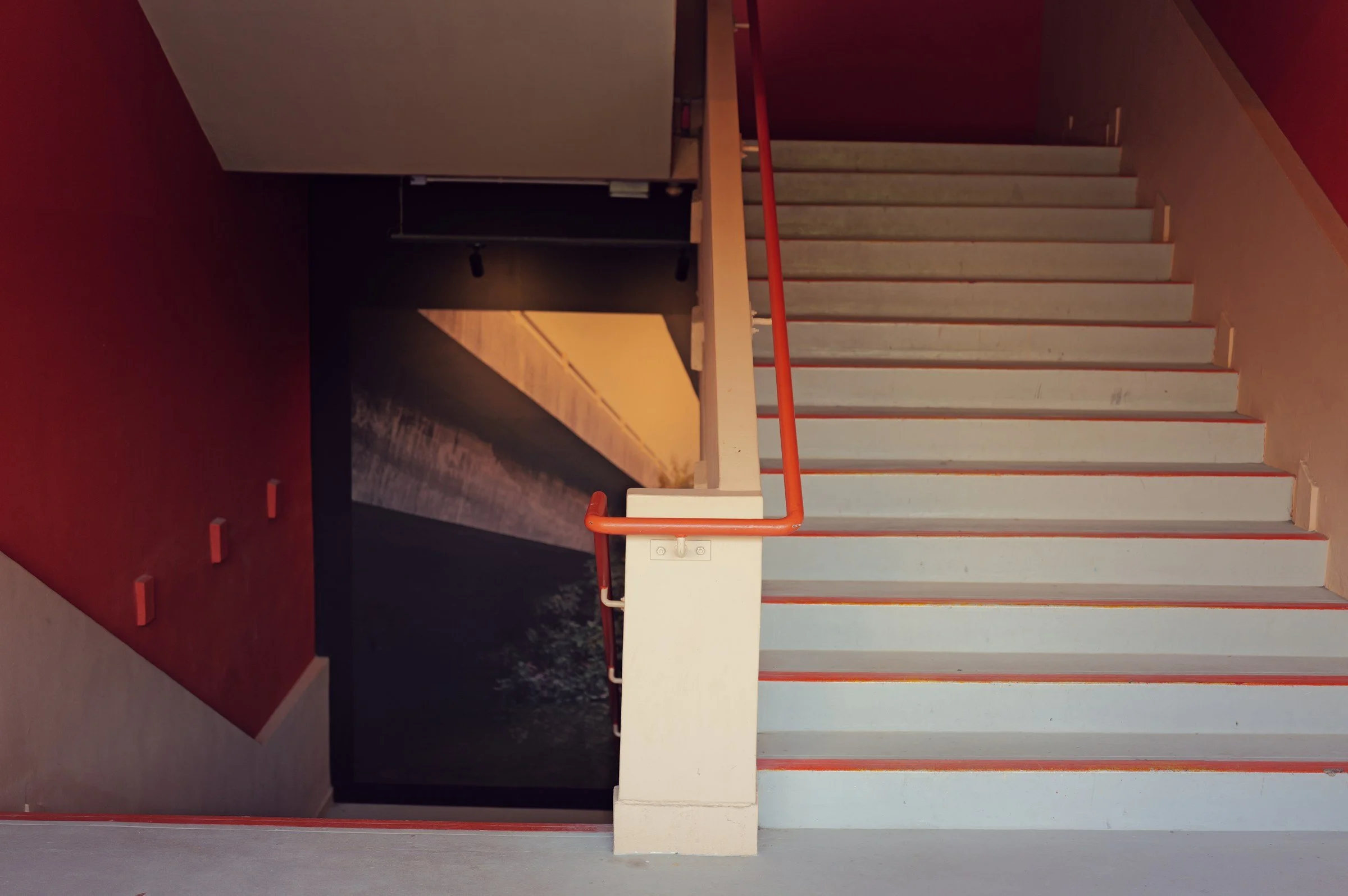White stairs and red walls frame a pool of warm light at New Bahru.