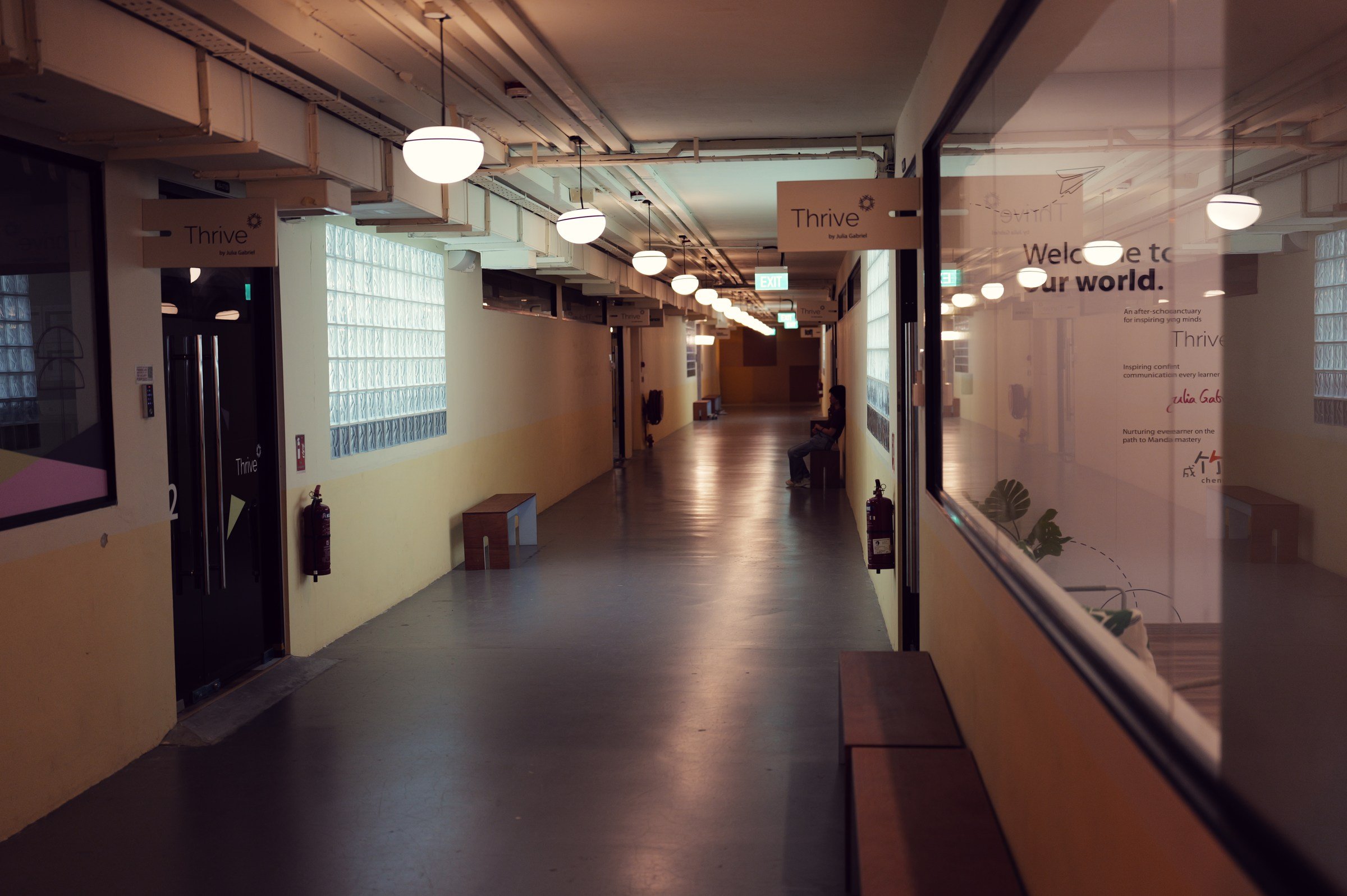 Long former school corridor with round pendant lights and shopfronts at New Bahru.