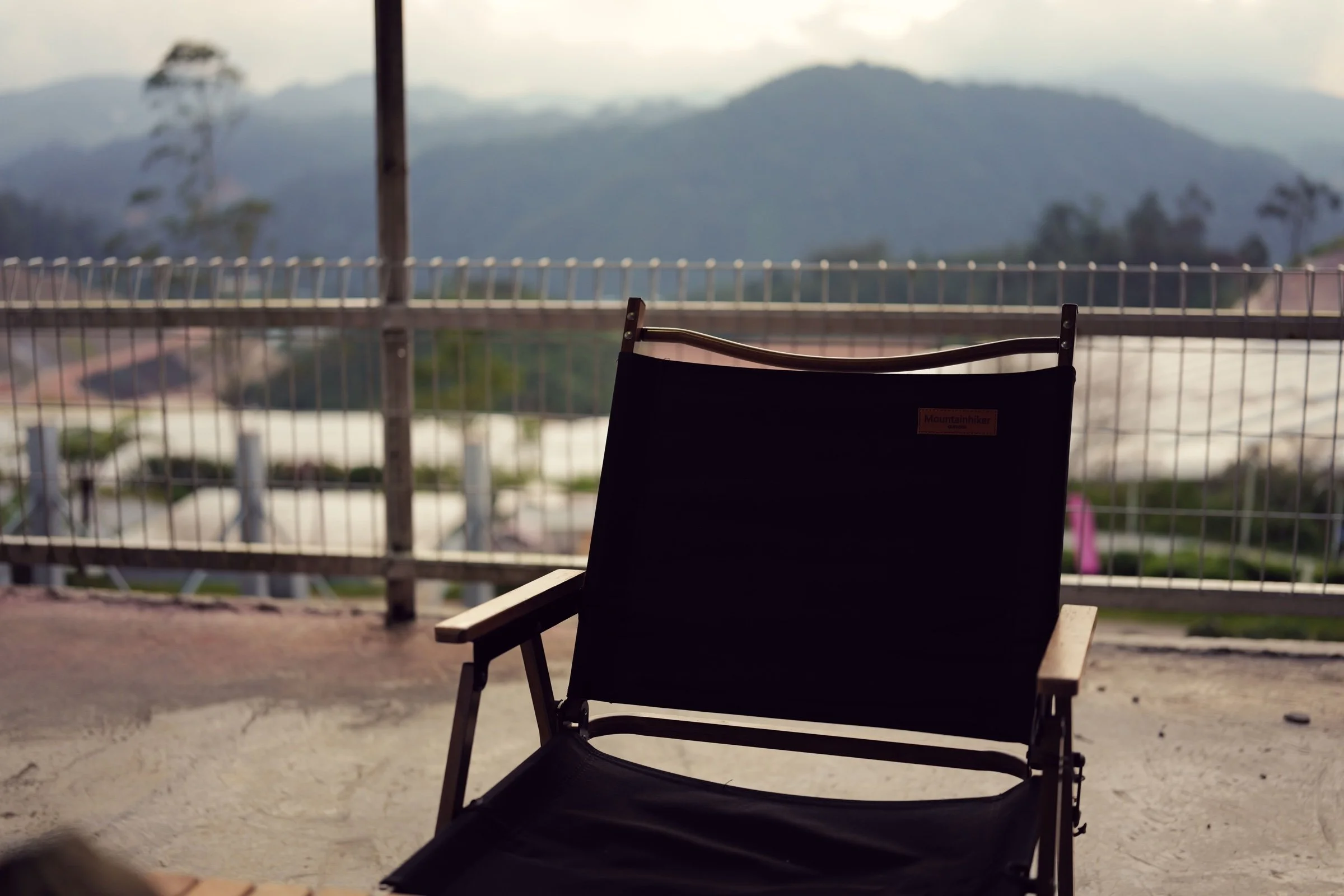 An empty folding chair overlooks mountain ridges from a sheltered terrace.