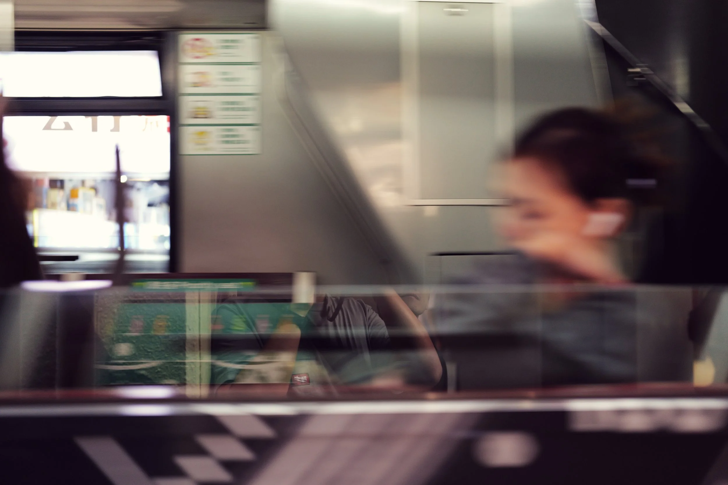 Blurred image showing an indoor setting with digital screens, signage, and reflections of people.
