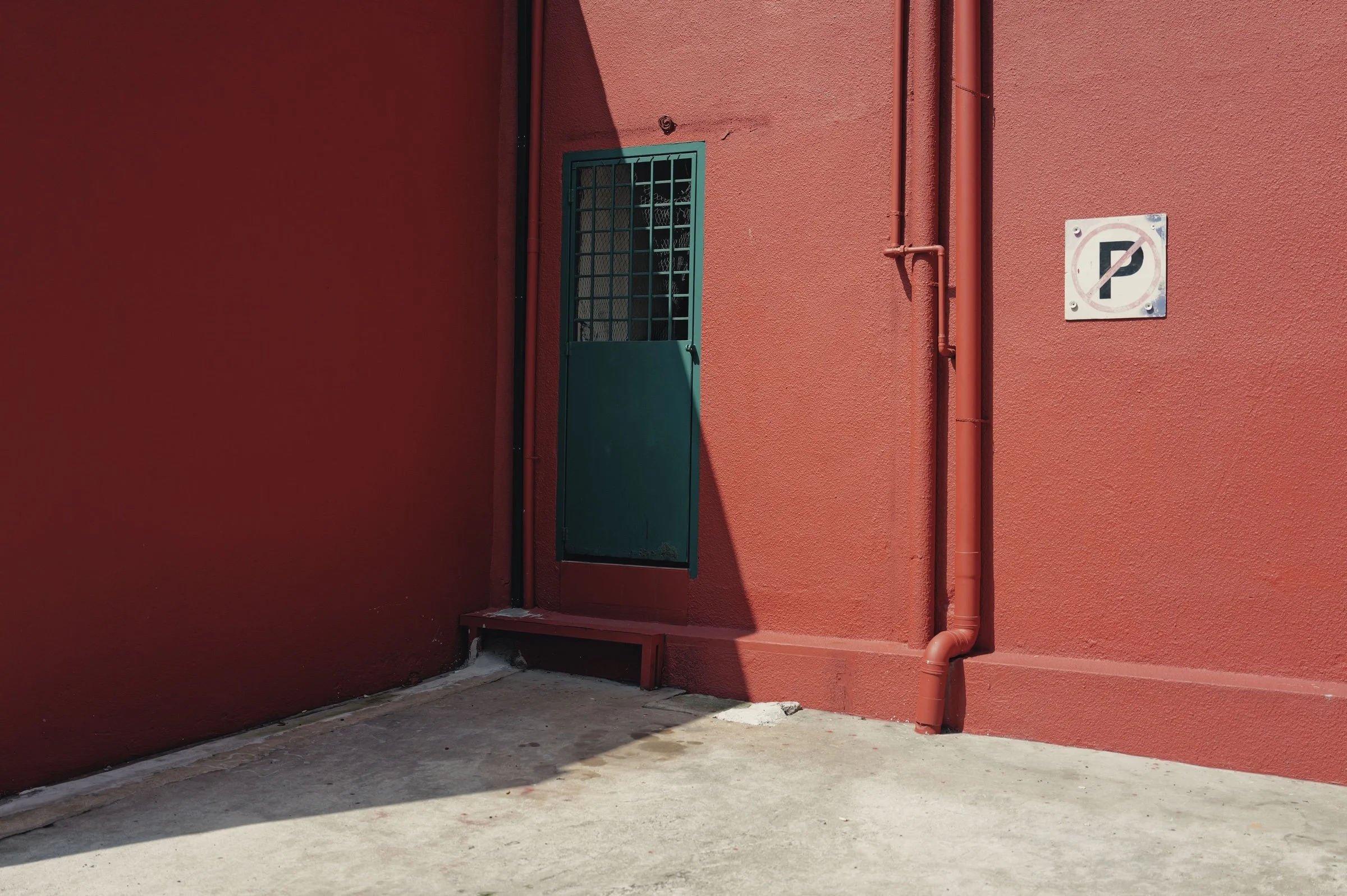 Hard sunlight casts an angular shadow across a red wall and green door.
