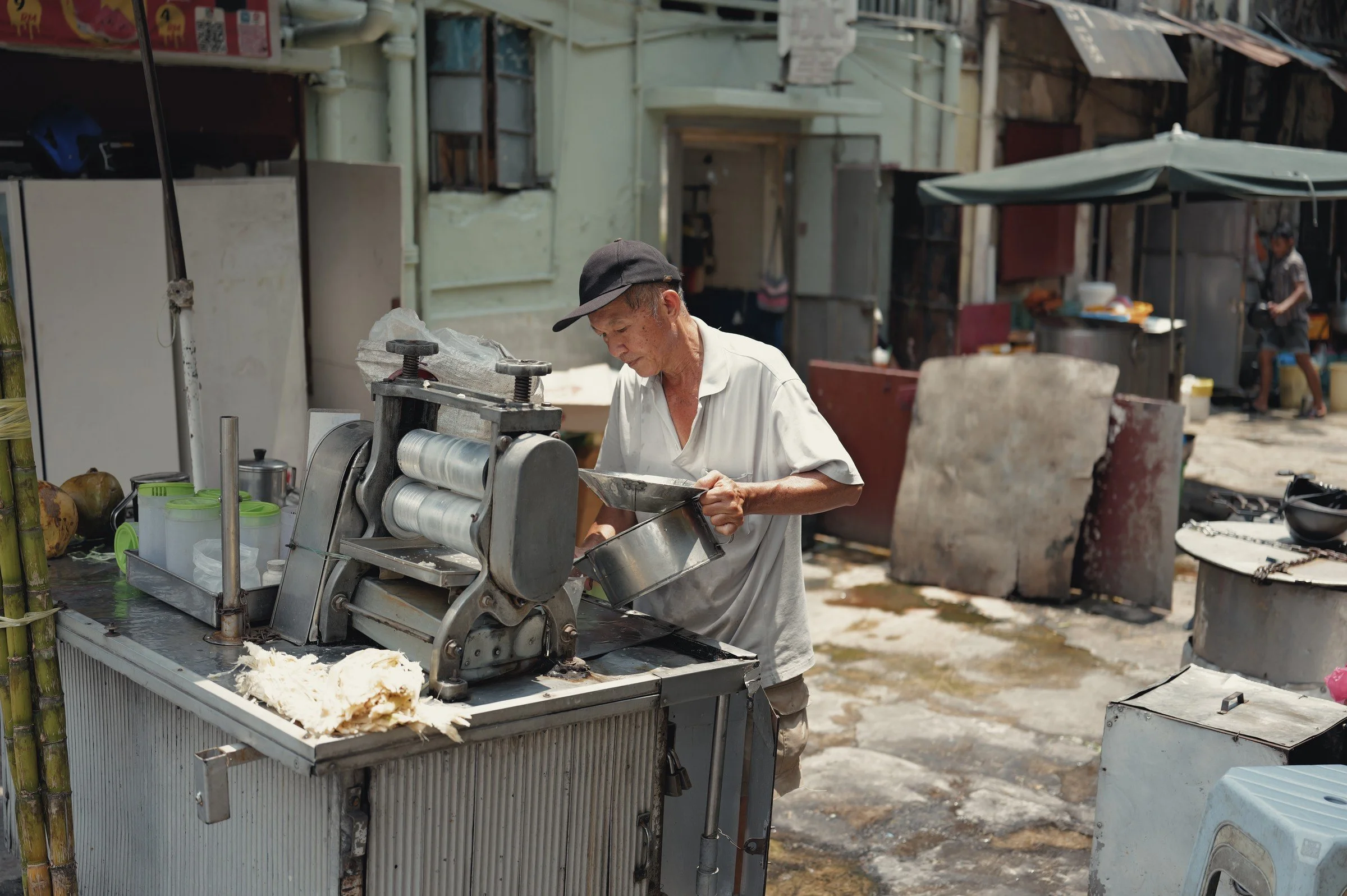 A street vendor works beside a metal food-preparation machine in an alley.