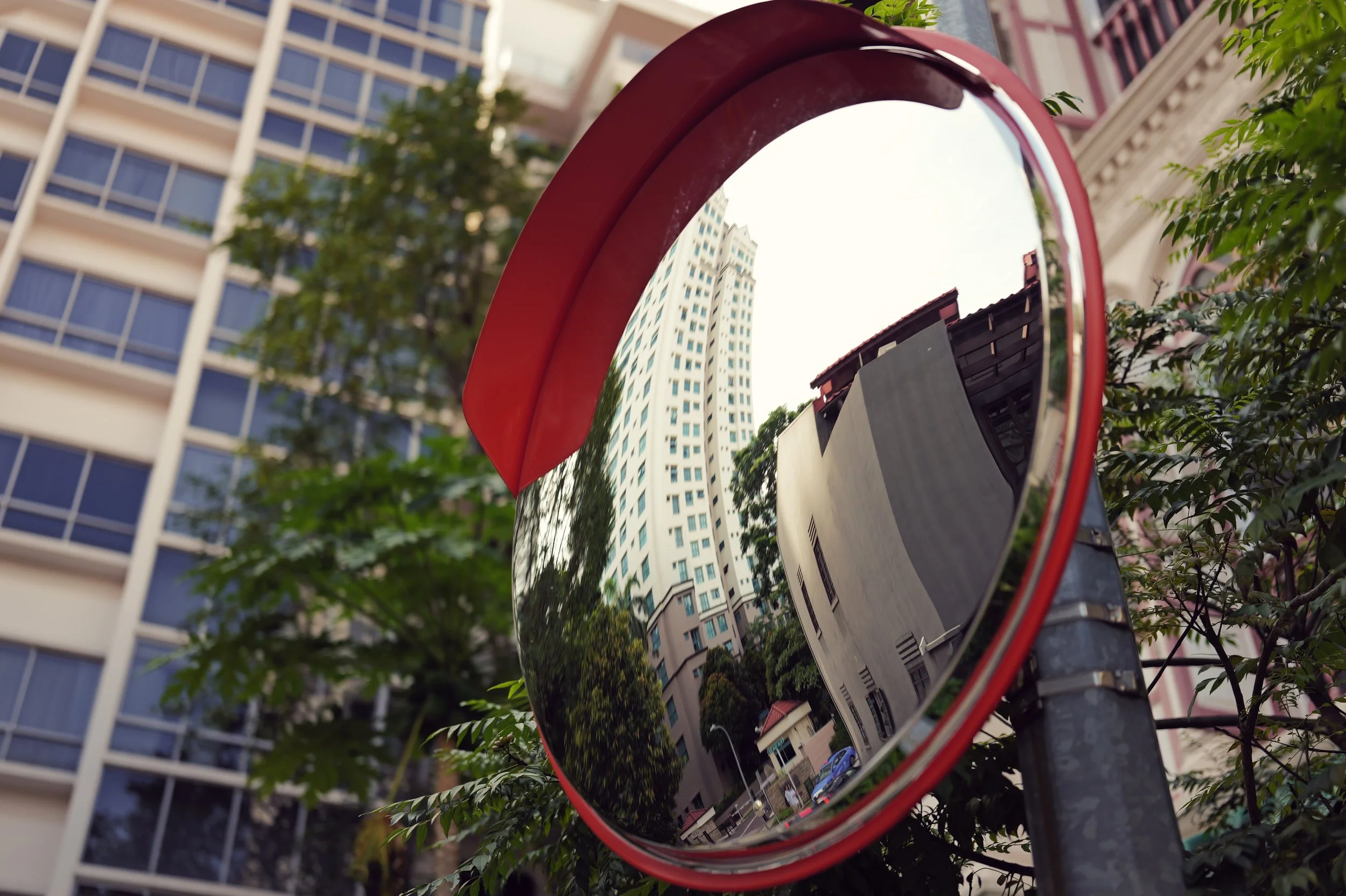 A convex traffic mirror reflects multistory apartment buildings and trees in an urban environment.