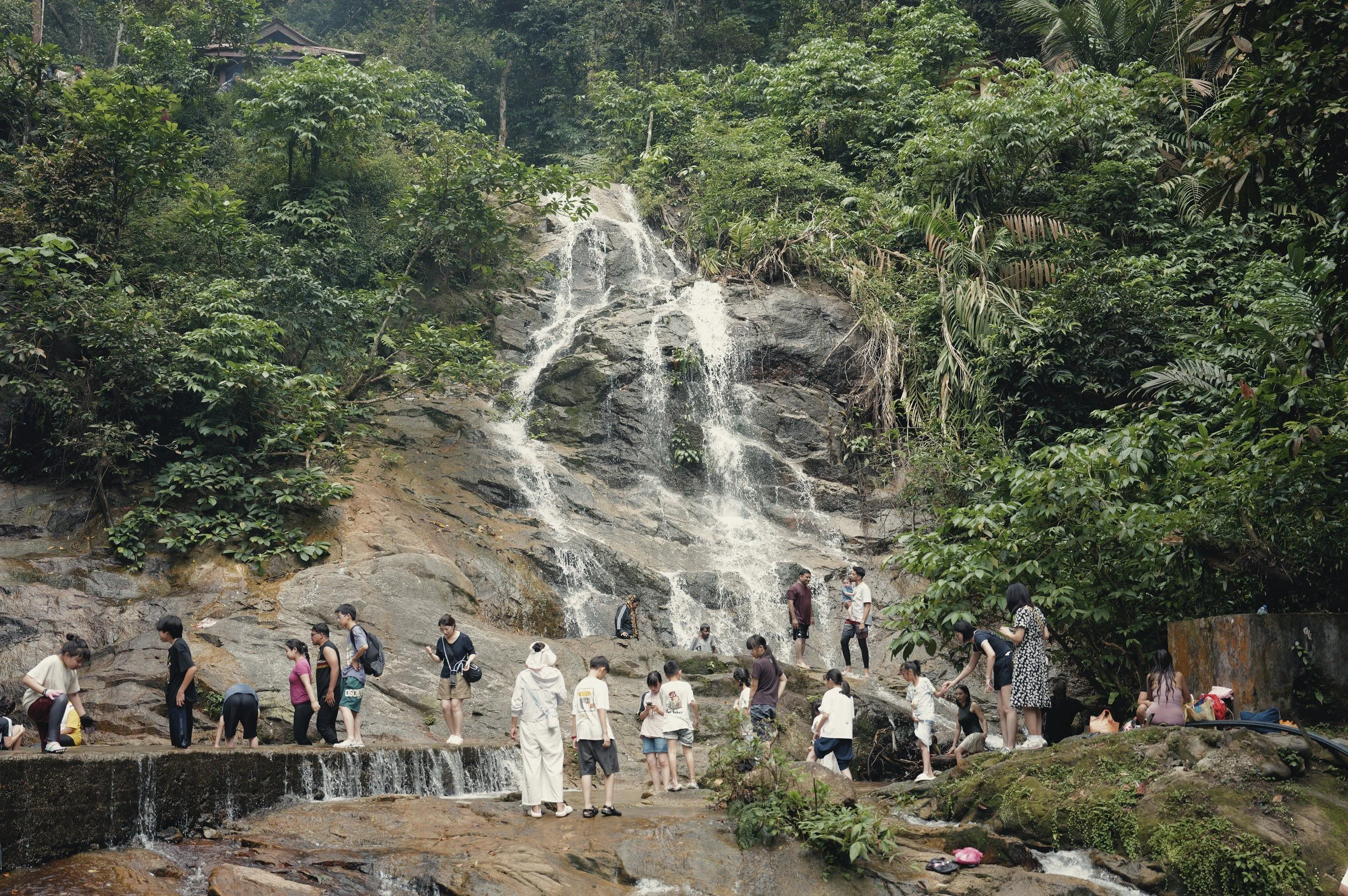 Visitors gather below a waterfall spilling down a broad rock face.