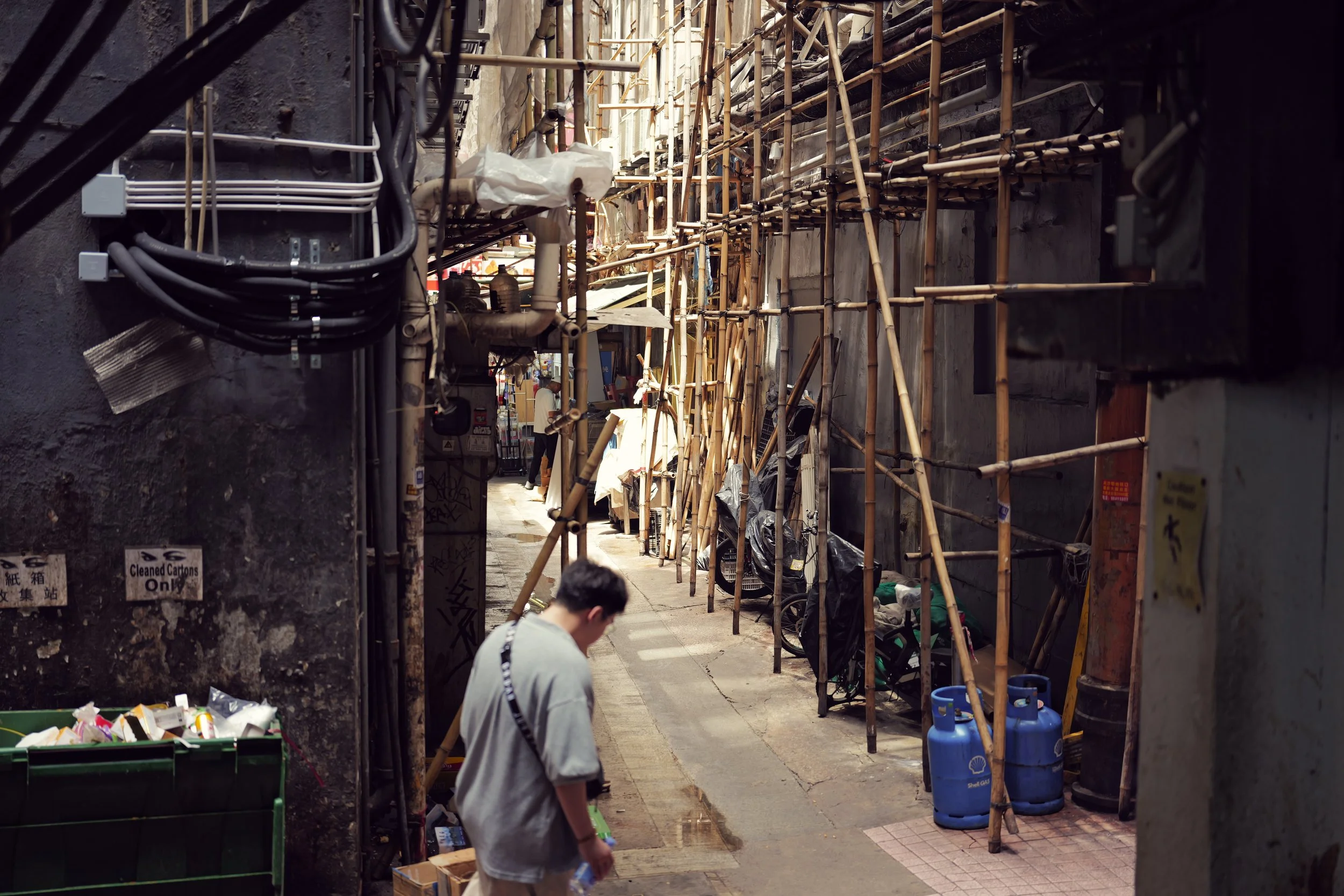 Street alleyway with scaffolding, pipes, and construction materials. People shopping or browsing in the area.