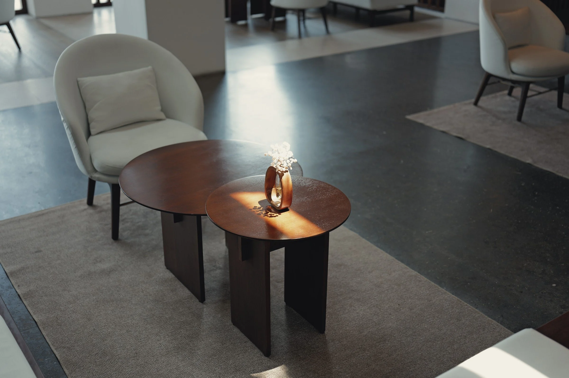 Sunlight falls across a small wooden table and pale armchairs in a quiet lounge.