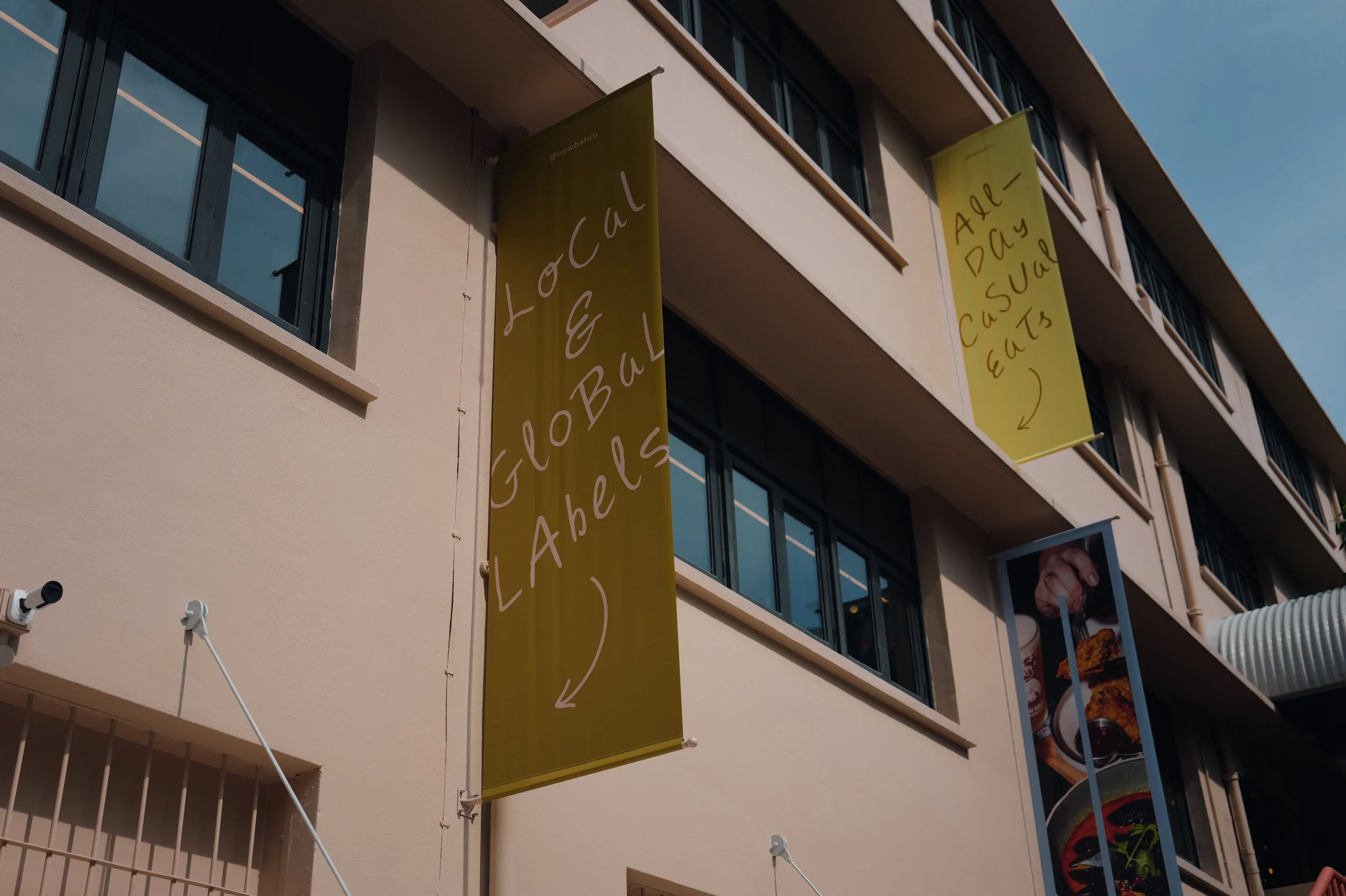 A beige building with multiple windows and two vertical banners hanging from the balconies. One banner has the text "Global Call" and the other "All Day – Casual EATS".